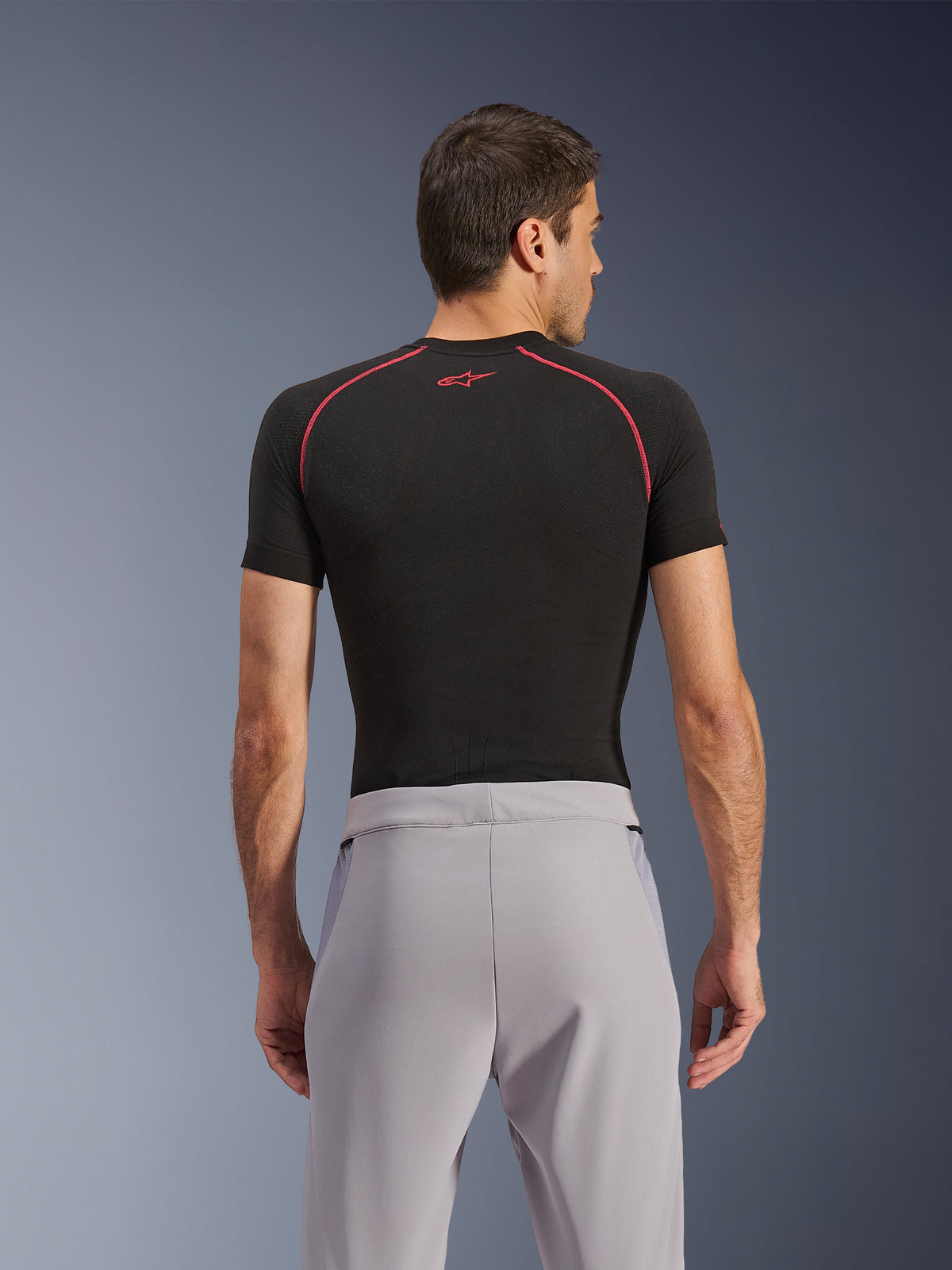 Pantaloni Alpinestars Aeroshell Airflow, Mid Gray, vista posteriore, indossati con un base layer nero a maniche corte con cuciture e logo rossi, caratterizzati da tessuto softshell elastico leggero e pannelli in rete per la massima ventilazione, vestibilità sportiva ergonomica per la guida della moto