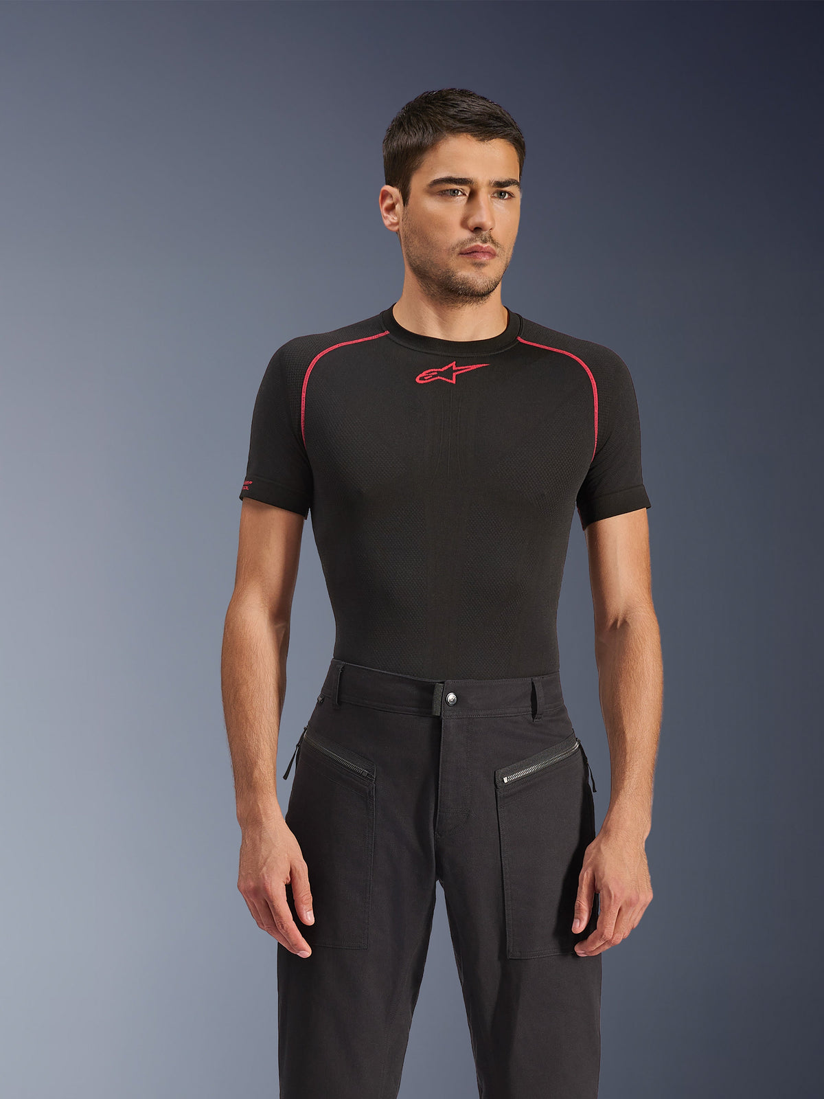 Modello maschile che indossa i pantaloni Alpinestars Flex-AST Canvas in nero, pantaloni da moto urbani con tasche anteriori con cerniera a vista e design d'ispirazione workwear, abbinati a un base layer nero con accenti rossi.