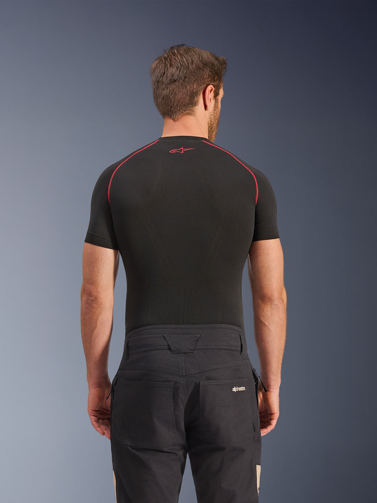 Alpinestars Flex-AST Canvas Pants in Black Aluminum, vista posteriore su modello, pantaloni da moto urbani di ispirazione workwear con logo sulla tasca posteriore, abbinati a un base layer nero a maniche corte con cuciture rosse.