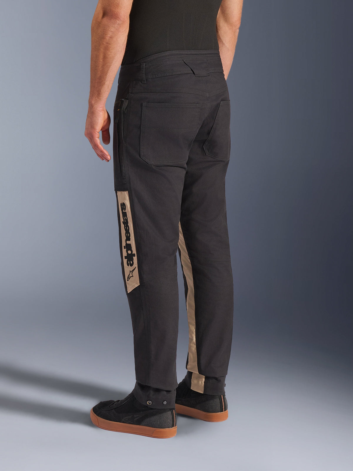 Pantaloni Alpinestars Flex-AST Canvas in Black Aluminum, vista posteriore che mostra pantaloni da moto urban con ampie tasche ispirate al workwear e pannelli verticali sulle gambe color tan con marchio Alpinestars.