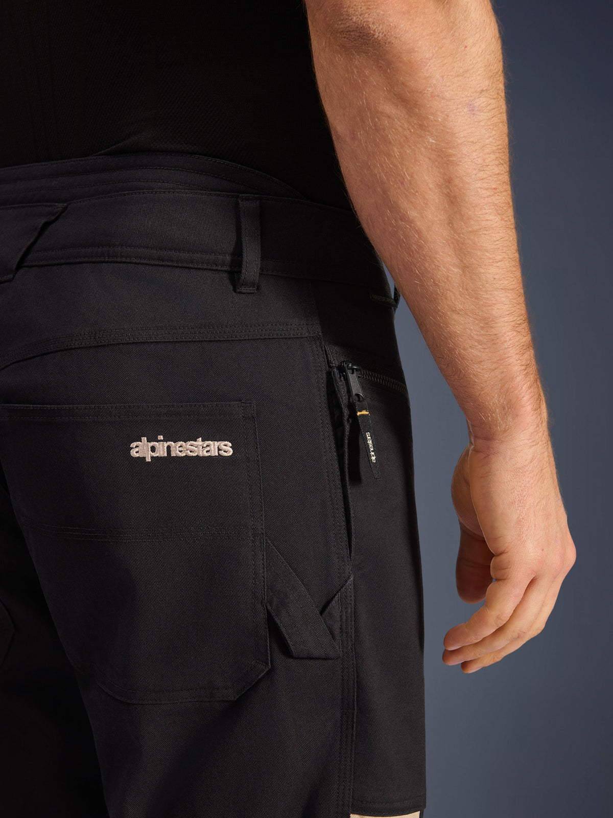 Pantaloni Alpinestars Flex-AST Canvas, pantaloni da moto urbani, Black Aluminum, primo piano delle tasche posteriori e laterali con logo Alpinestars ricamato, tasca con cerniera e tirazip brandizzato, costruzione in resistente twill di tela elasticizzata.