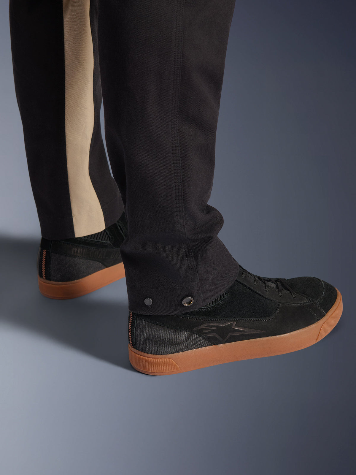 Pantaloni Alpinestars Flex-AST Canvas in Black Aluminum, primo piano della parte inferiore della gamba con regolazioni a pressione e striscia verticale color alluminio, abbinati a sneakers da moto nere con suola gum, abbigliamento moto urbano.