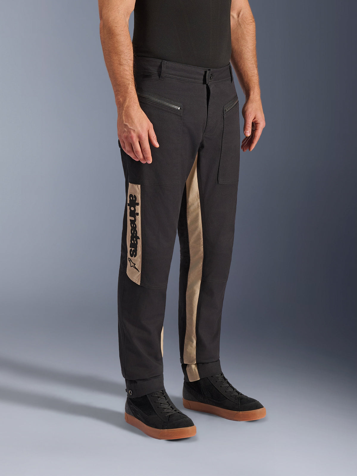 Alpinestars Flex-AST Canvas Pants, pantaloni moto urbani, Black Aluminum, con pannelli laterali color sabbia e logo Alpinestars verticale, design ispirato al workwear con tasche con zip e taglio ergonomico, indossati con sneakers nere casual per un look urbano moderno.