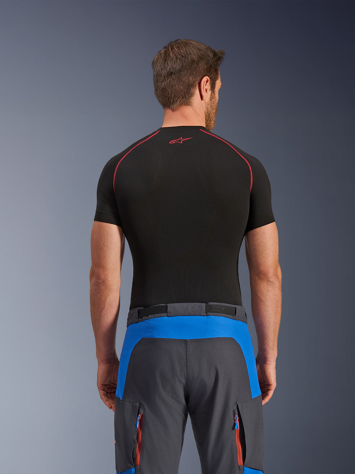 Pantaloni Alpinestars Maxdura Dual, pantaloni da moto adventure, blu reale e grigio scuro, vista posteriore, indossati con un base layer nero a maniche corte, con pannelli blu sulla parte posteriore e tasche cargo con zip arancioni, abbigliamento tecnico per guida dual-sport