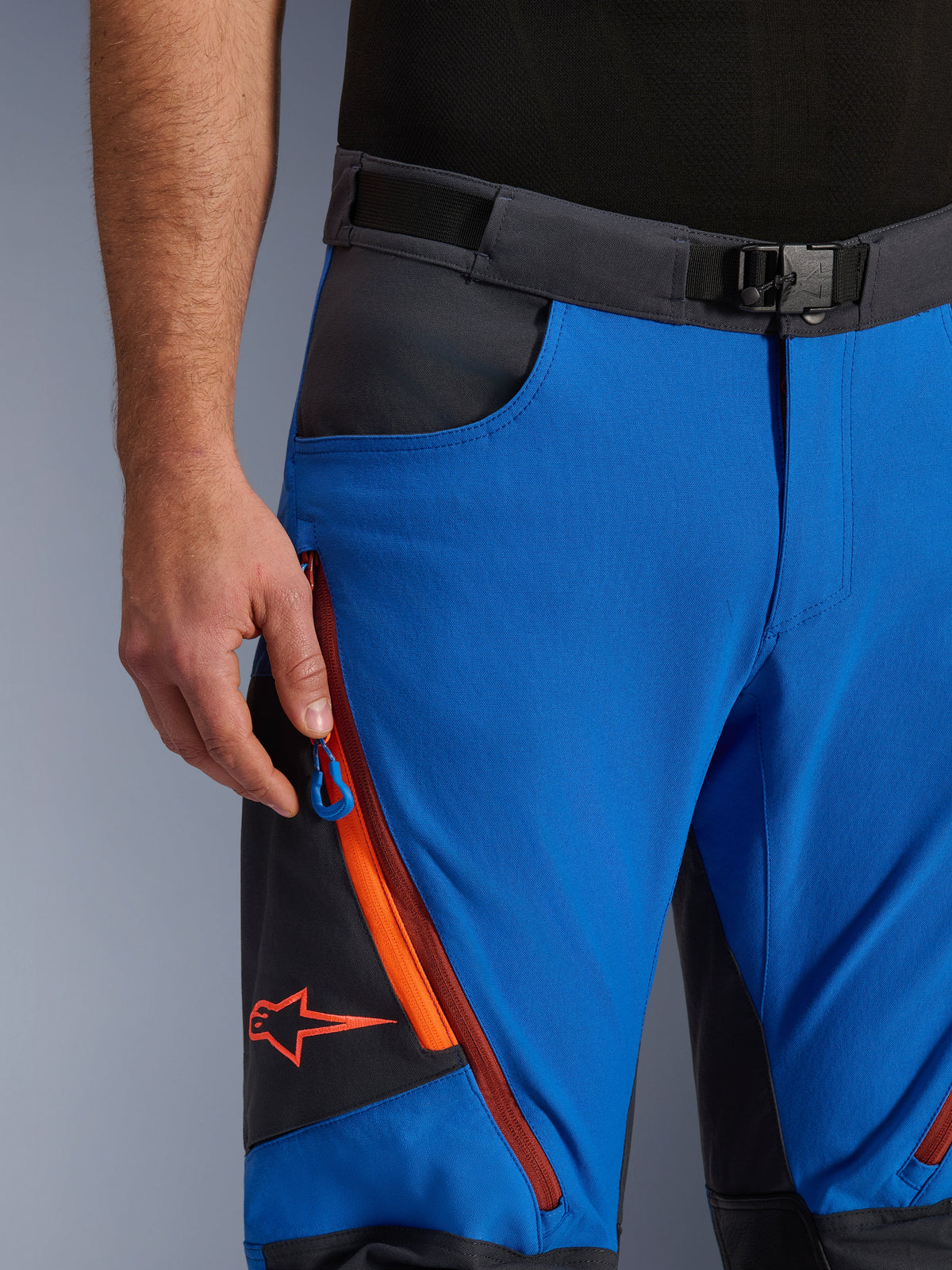 Alpinestars Maxdura Dual Pants in Royal Blue e Deep Gray, vista ravvicinata del girovita con fibbia magnetica, tasca cargo con zip e dettagli arancioni, logo Alpinestars rosso, abbigliamento tecnico da moto per avventura