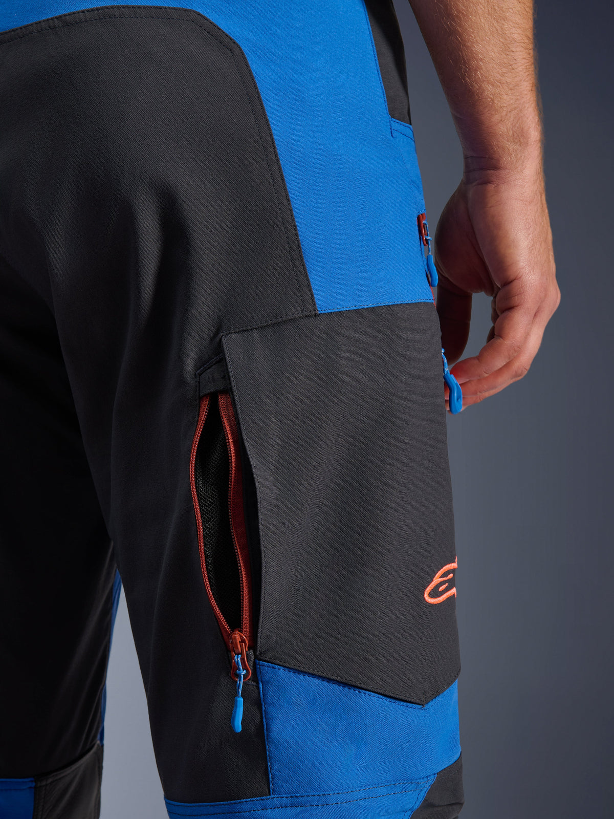 Alpinestars Maxdura Dual Pants, blu reale e grigio scuro, primo piano della tasca cargo laterale con cerniera, tiranti delle zip blu, logo ricamato arancione, abbigliamento da motociclismo adventure