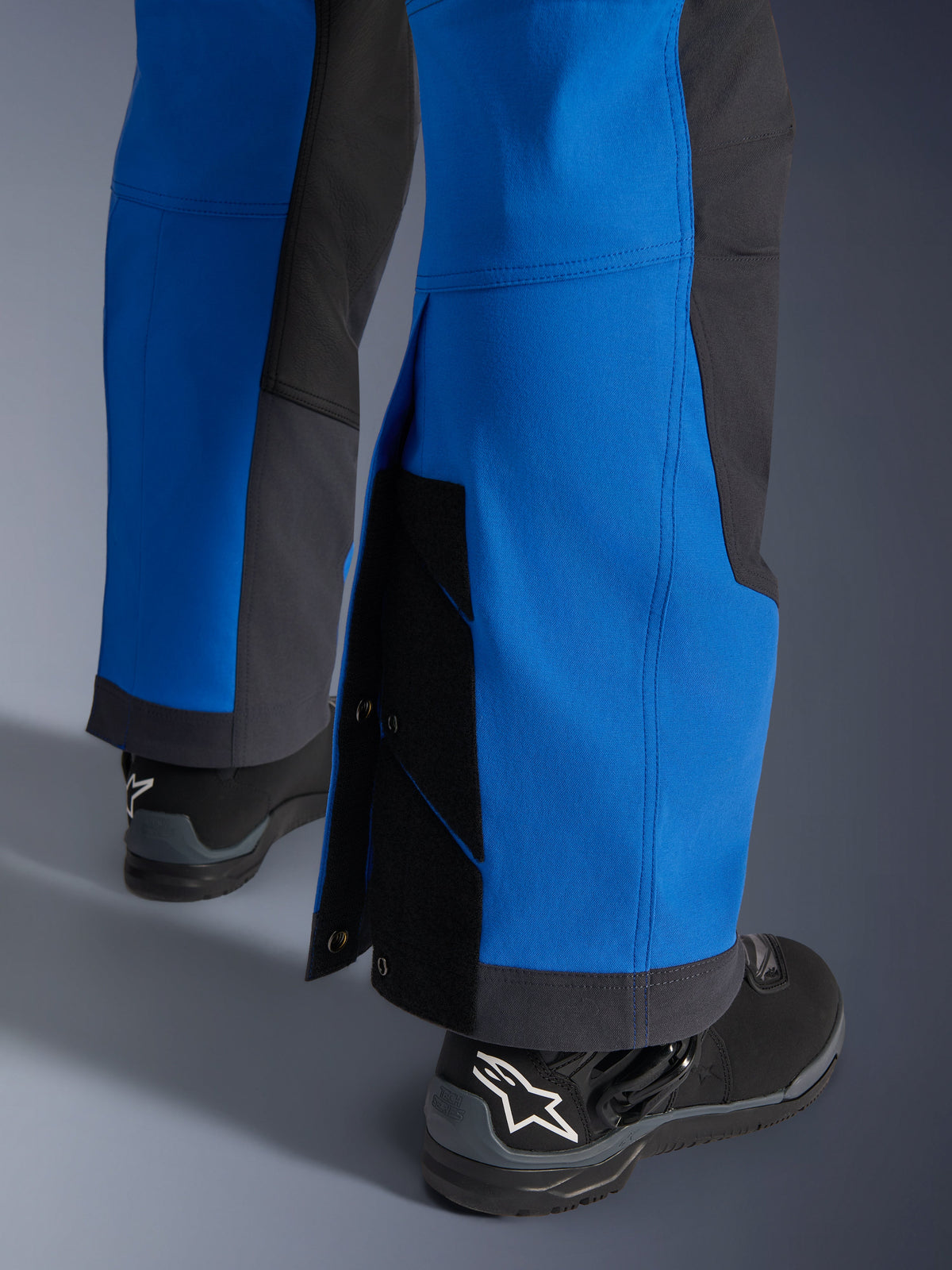 Alpinestars Pantaloni Maxdura Dual, blu royal e grigio scuro, primo piano della parte inferiore della gamba regolabile con chiusure a scatto e tassello, design con vestibilità adventure sopra lo stivale, indossati con stivali da moto Alpinestars neri