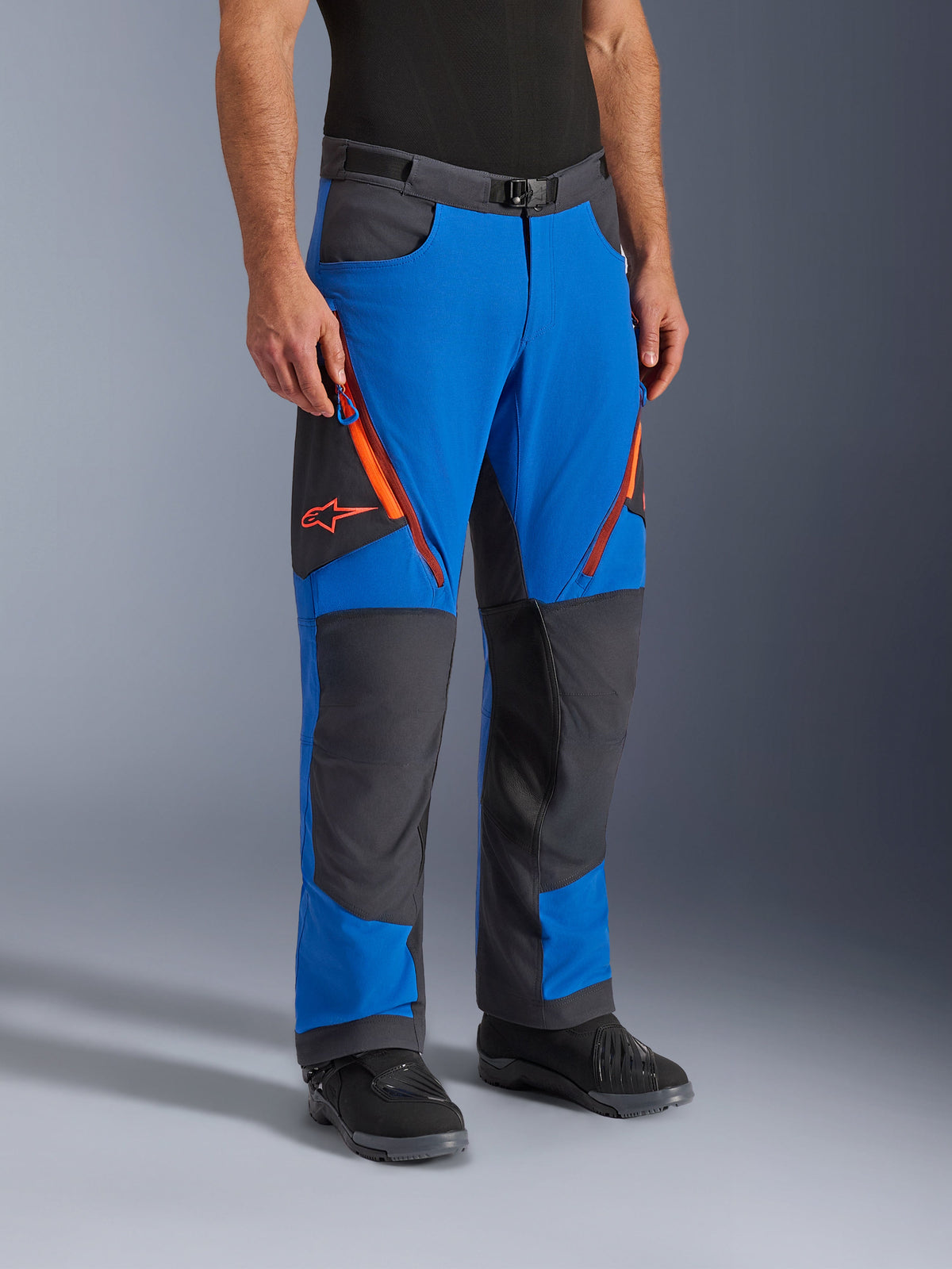 Alpinestars Maxdura Dual Pants, pantaloni da moto adventure, blu reale e grigio scuro con dettagli arancioni, caratterizzati da prese d'aria con zip sulle cosce, pannelli rinforzati sulle ginocchia e cintura con fibbia magnetica, design tecnico sopra-stivale per guida dual-sport.