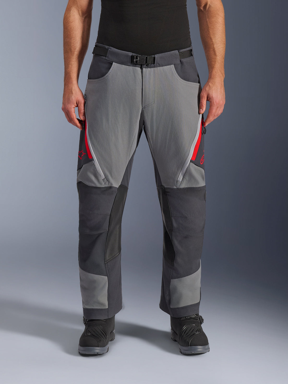 Pantaloni Alpinestars Maxdura Dual, pantaloni da moto adventure, grigio scuro e grigio intenso con accenti rossi, vista frontale che mostra le prese d'aria con cerniera sulle cosce, cintura con fibbia magnetica e pannelli rinforzati sulle ginocchia, design over-boot per guida dual-sport.