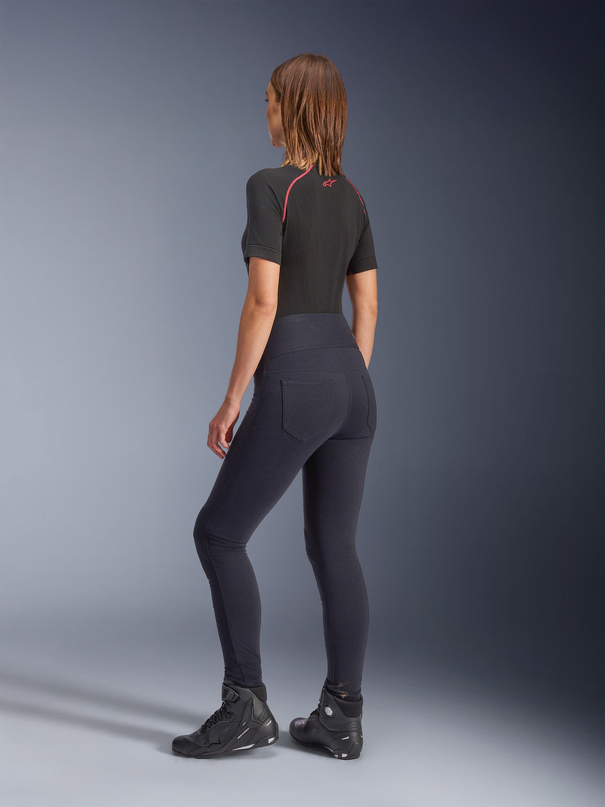 Leggings Alpinestars Stella Flex-Ast da donna, nero, vista posteriore con vestibilità a vita alta e tasche posteriori, indossati con base layer nero a maniche corte con dettagli rossi e scarpe da moto nere, abbigliamento da moto urban contemporaneo