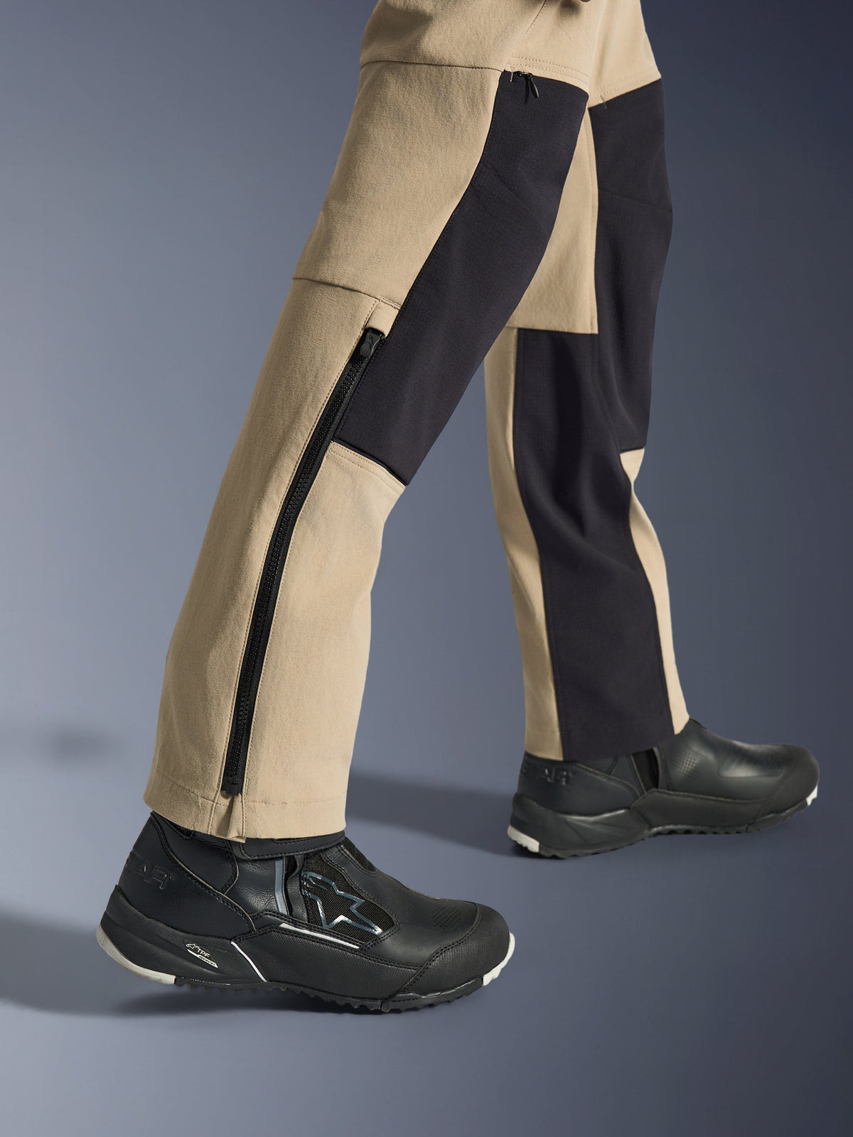 Alpinestars Pantaloni Stella Flex-AST Explorer da donna, pantaloni da moto adventure, sabbia e nero, vista ravvicinata della parte inferiore delle gambe e delle caviglie con una lunga cerniera laterale e pannelli di rinforzo neri, indossati con scarpe da moto Alpinestars nere.