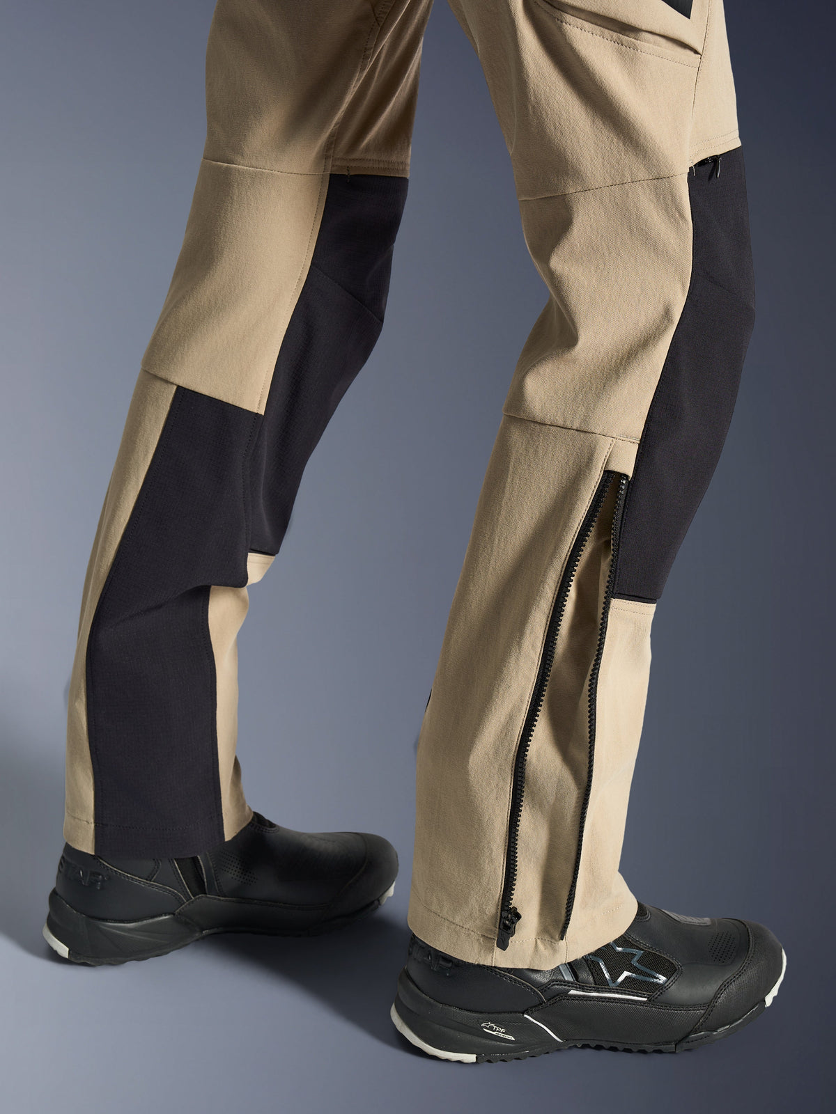 Alpinestars Stella Flex-AST Explorer Pants, pantaloni da moto da donna, sabbia e nero, primo piano della parte inferiore delle gambe che mostra l'orlo con cerniera per la calzata dello stivale, indossati con scarpe da moto Alpinestars nere, con pannelli in resistente ripstop e tessuto elasticizzato traspirante.