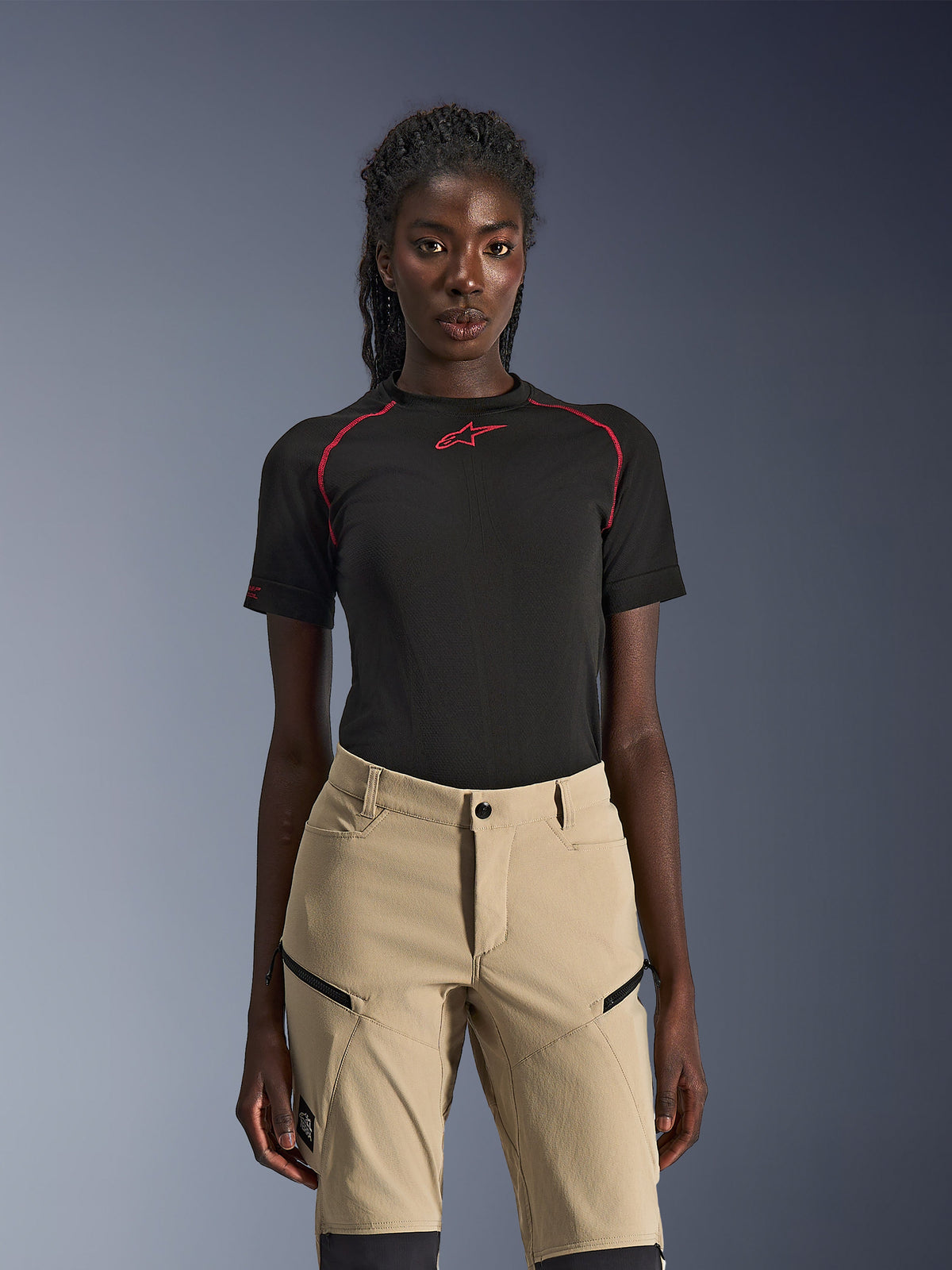 Alpinestars Stella Flex-AST Explorer Pants, pantaloni da moto da donna color sabbia, indossati con un top tecnico nero a maniche corte con cuciture rosse, abbigliamento da adventure touring con tasche cargo con zip e resistente tessuto ripstop.
