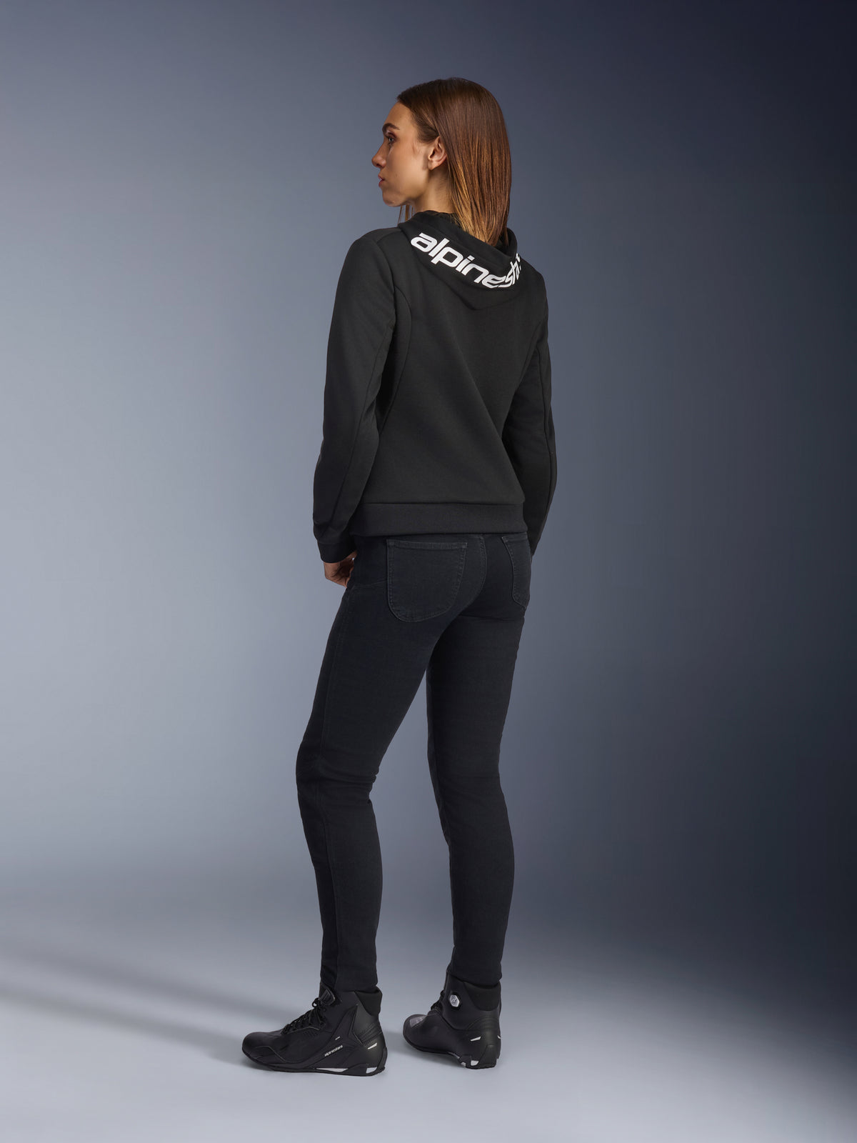 Alpinestars Daisy V3 Women's Riding Denim, pantaloni da moto da donna, Rinse Black, vista posteriore che mostra la vestibilità slim e la vita alta, abbinati a una felpa Alpinestars nera e stivali da moto per un look urban