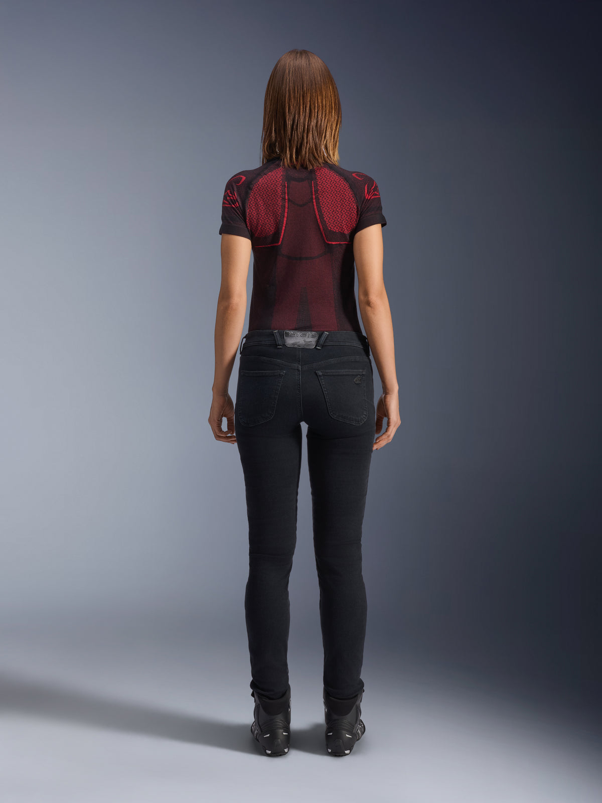Alpinestars Daisy V3 Women's Riding Denim, Rinse Black, pantaloni da moto slim fit visti da dietro, con design a vita alta e tasche posteriori, abbinati a maglia tecnica rossa e nera e stivali neri, abbigliamento moto urban da donna