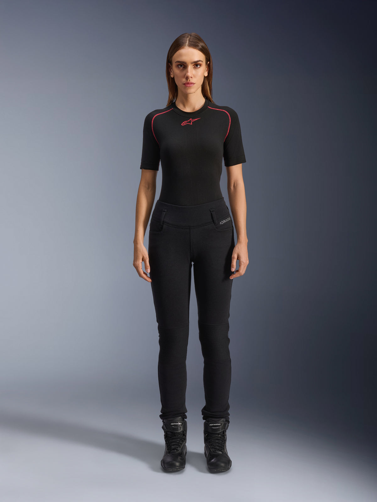 Alpinestars Leggings Banshee Donna, leggings da moto neri, vestibilità anatomica aderente, indossati da una modella con base layer nero e stivali da moto, con pannelli a costine sulle ginocchia e struttura a vita alta per la guida urbana