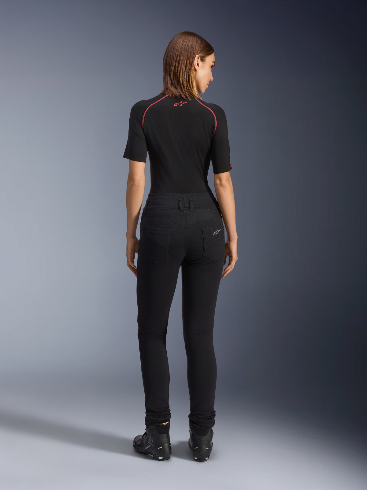 Leggings Banshee Donna Alpinestars, leggings da moto neri, vista posteriore che mostra la vestibilità aderente e il tessuto elasticizzato anatomico, con tasche posteriori e dettaglio del logo, indossati con un base layer nero e scarpe da guida, abbigliamento moto urban per donna