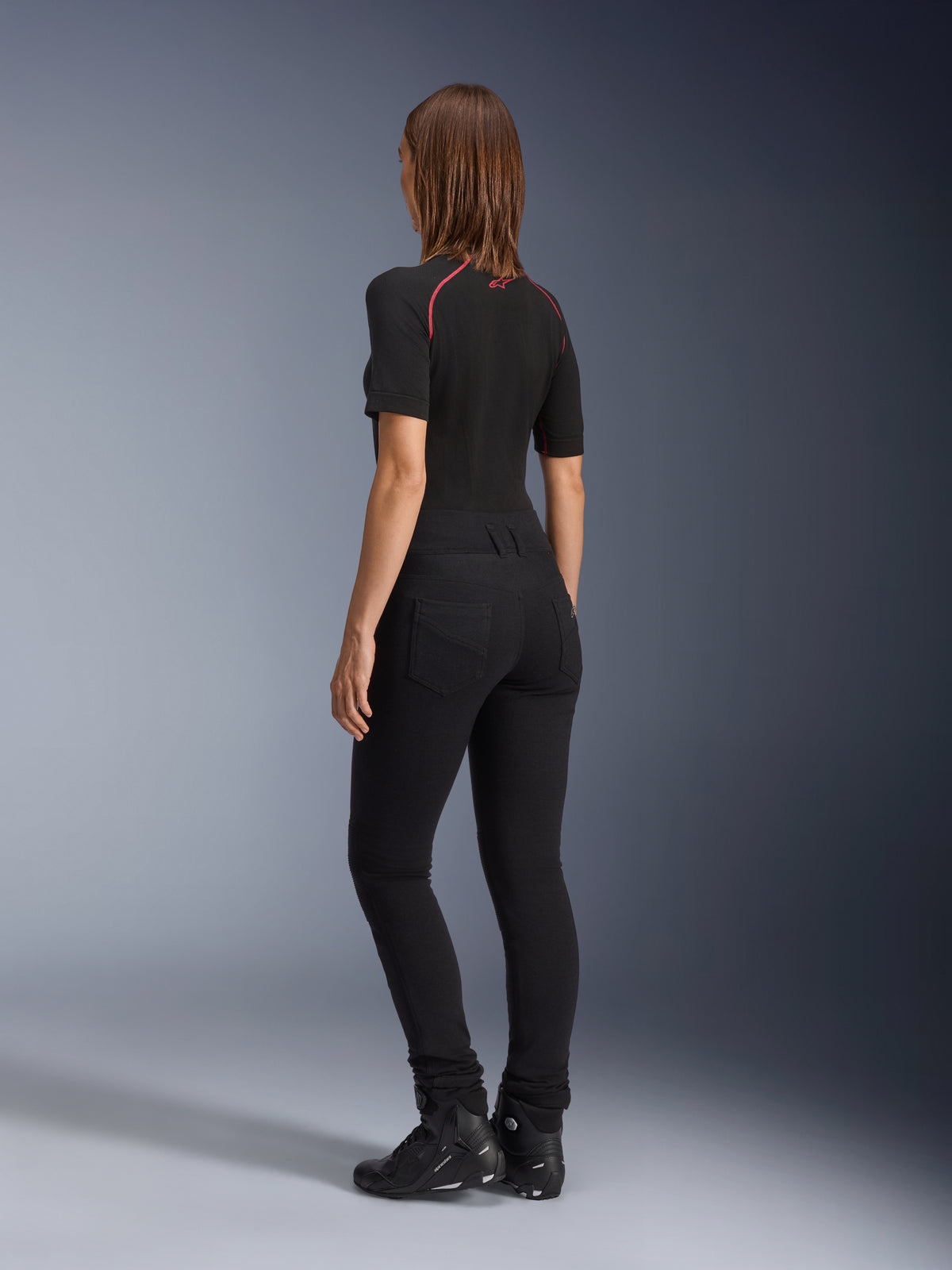Alpinestars Leggings Banshee Donna, nero, vista posteriore con vestibilità anatomica elasticizzata e tasche posteriori, indossati con maglia nera a maniche corte e stivali da moto, abbigliamento urban elegante da motociclismo per donna