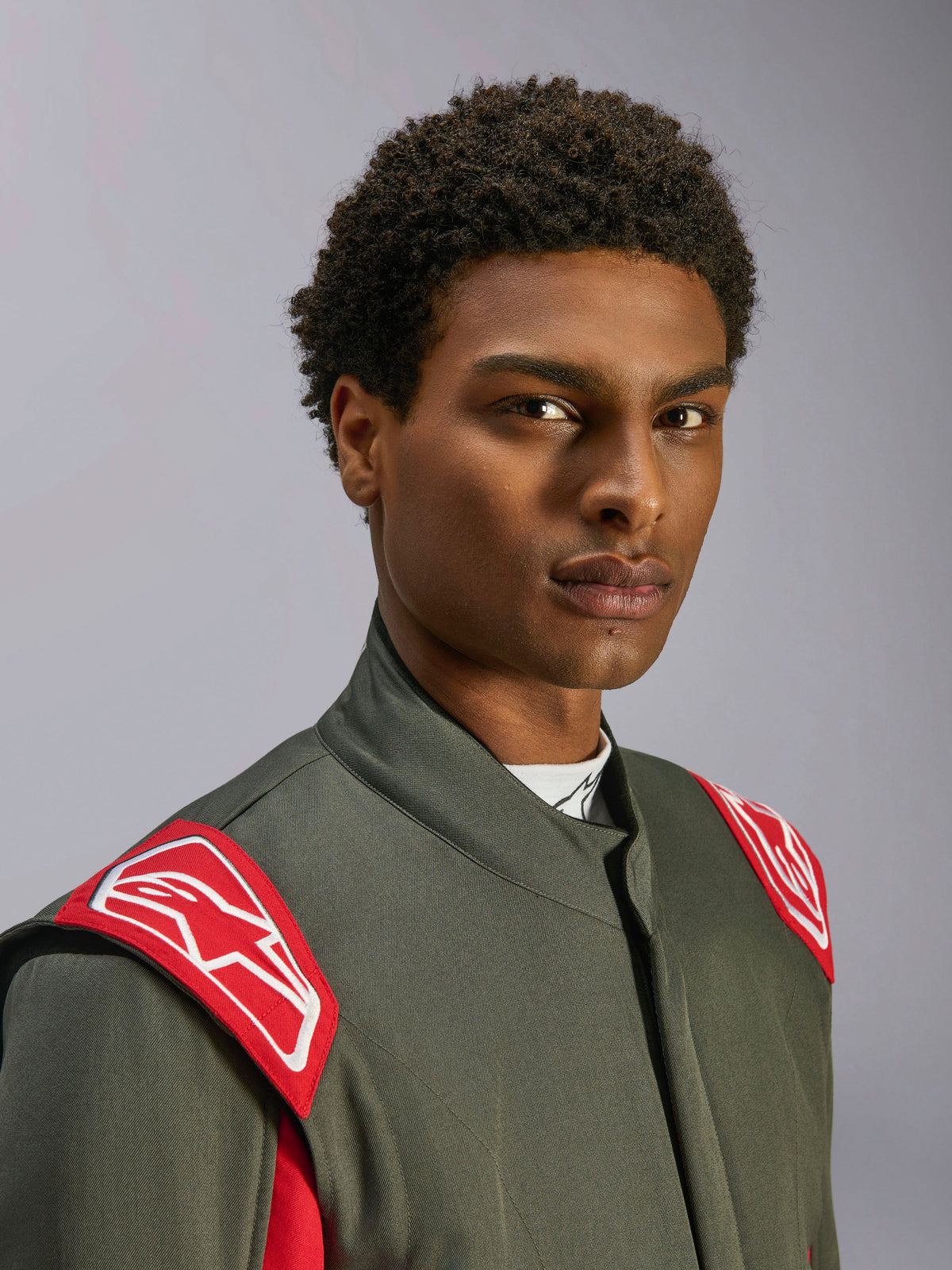 Alpinestars GP Race V3 Suit FIA, tuta da corsa auto, Antracite Rosso, primo piano della parte superiore del busto e della testa, caratterizzata da spalline rosse con logo Alpinestars bianco, colletto alto e materiale in twill grigio