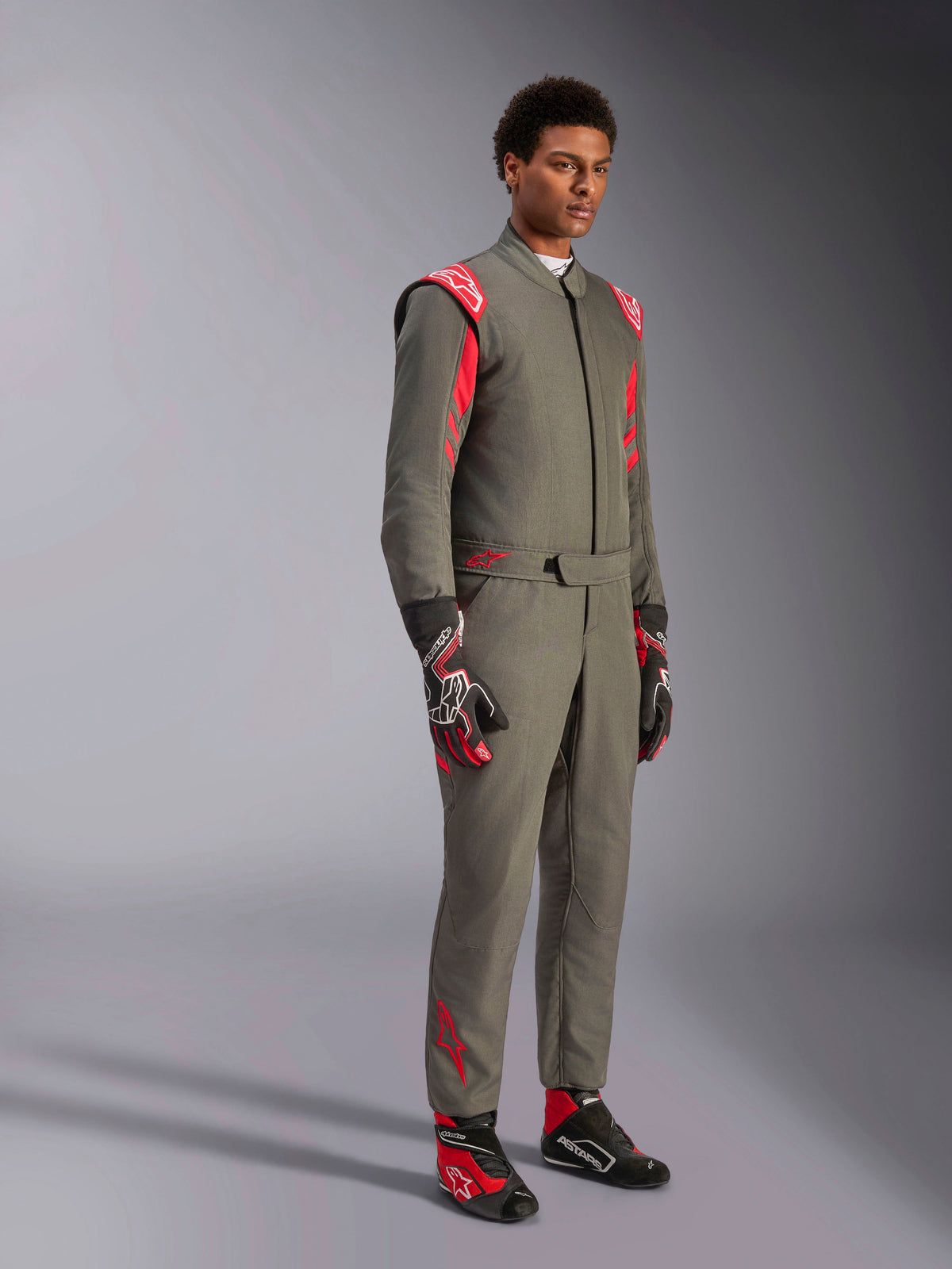 Alpinestars GP Race V3 Suit FIA, tuta da corsa auto antracite e rosso, indossata con guanti e scarpe da corsa abbinati, con spalline e loghi rossi, elegante design tecnico a due strati per il motorsport