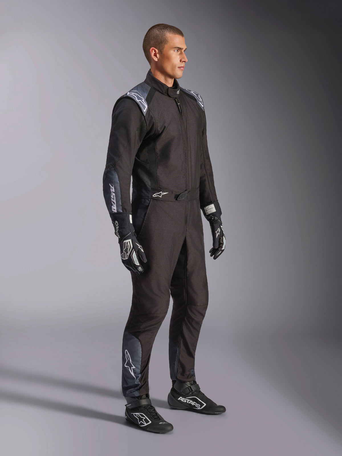 Tuta Alpinestars KMX-5 V3, tuta da kart in nero Dark Shadow, indossata con guanti e scarpe da corsa neri coordinati, dotata di traforazioni tagliate al laser e pannelli in mesh tecnico, elegante design a doppio strato con loghi bianchi per il motorsport professionale