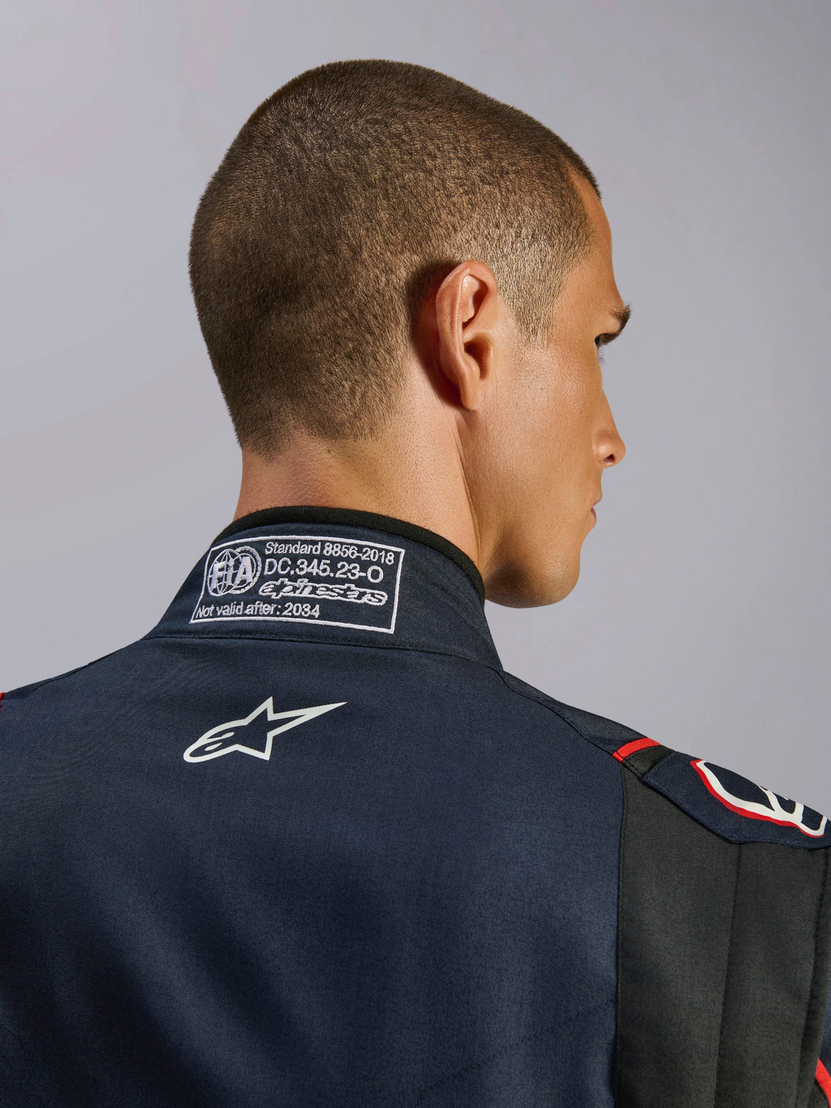 Tuta Alpinestars GP Tech V4 in blu navy, nero e rosso, primo piano del colletto posteriore con l'etichetta di certificazione FIA 8856-2018 e il logo Alpinestars ricamato in bianco, dettaglio di una tuta da corsa automobilistica ad alte prestazioni