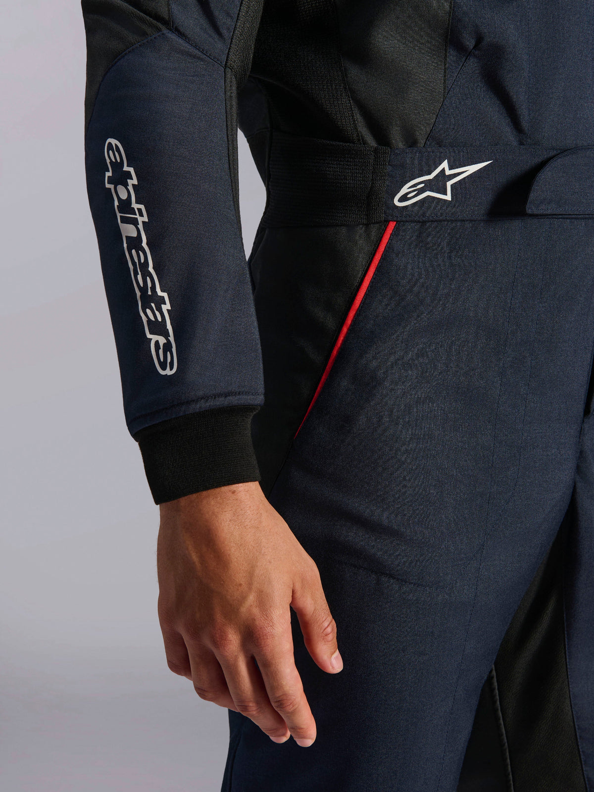 Tuta Alpinestars GP Tech V4 in blu navy, nero e rosso, dettaglio della vita e della manica con loghi Alpinestars bianchi, profili rossi e tessuto twill testurizzato.