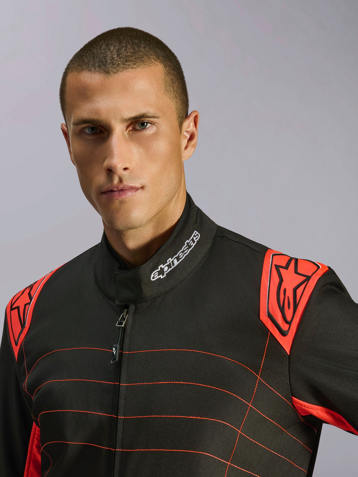Primo piano di un pilota con tuta Alpinestars KMX-9 V3 in nero e rosso fluo, logo ricamato sul colletto e spalline rosse con marchio Alpinestars, abbigliamento tecnico da karting