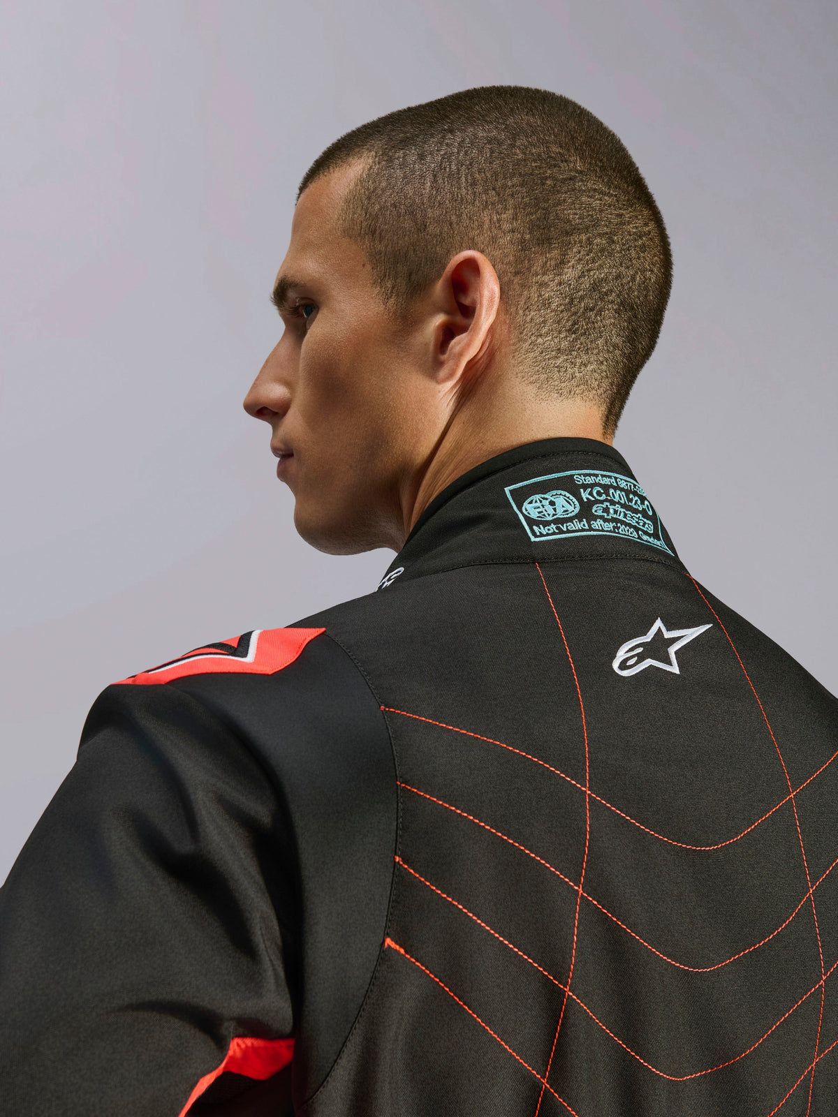 Tuta Alpinestars KMX-9 V3, tuta da kart nero e rosso fluo, vista ravvicinata della parte superiore della schiena e del colletto su un modello, con logo Alpinestars bianco, cuciture rosse elaborate ed etichetta di certificazione FIA sul collo