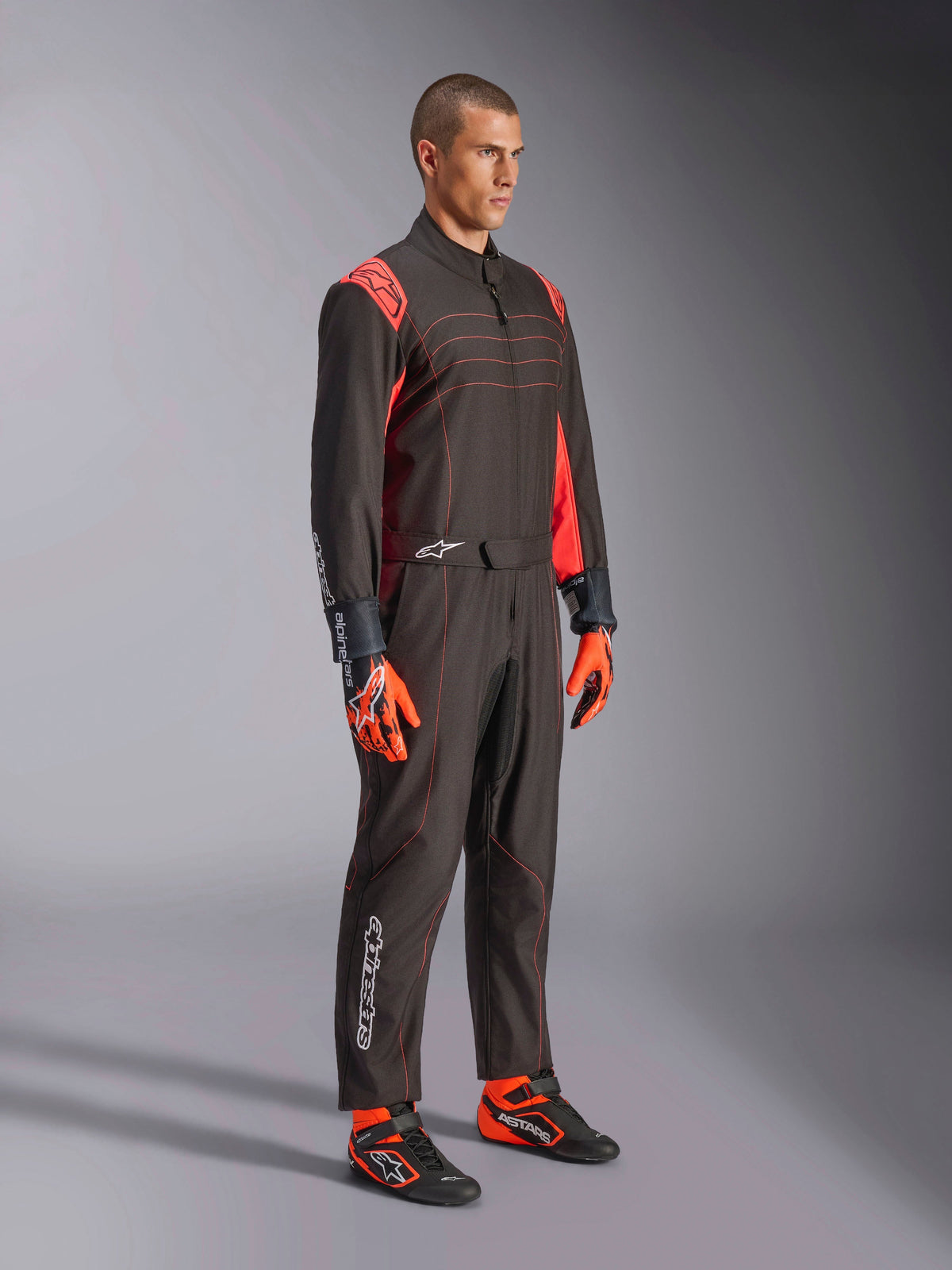 Alpinestars Tuta KMX-9 V3, tuta da karting, Nero Rosso Fluo, indossata da un modello con guanti arancioni e scarpe da corsa nere, con cuciture rosse, inserti sulle spalle e loghi bianchi, design atletico per corse professionali