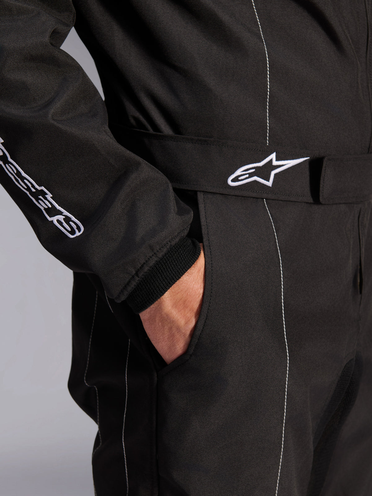 Tuta Alpinestars KMX-9 V3, nero e bianco, vista ravvicinata della cintura regolabile in vita con logo ricamato, tasca laterale, cuciture bianche a contrasto su tessuto nero, dettaglio tecnico della tuta da kart
