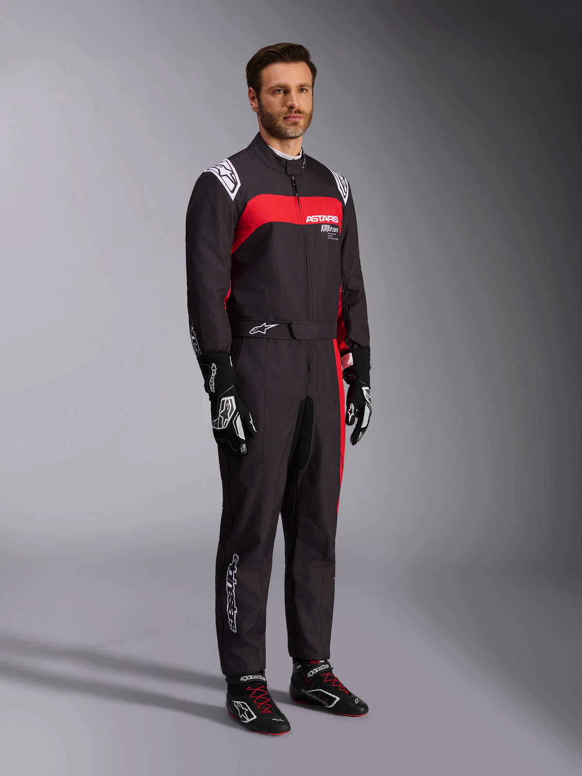 Modello che indossa la tuta Alpinestars KMX-9 V3 Graphic 3, tuta da kart, nero e rosso, con spalline bianche e logo rosso sul petto, abbinata a guanti da corsa neri e scarpe con lacci rossi, abbigliamento professionale per motorsport.