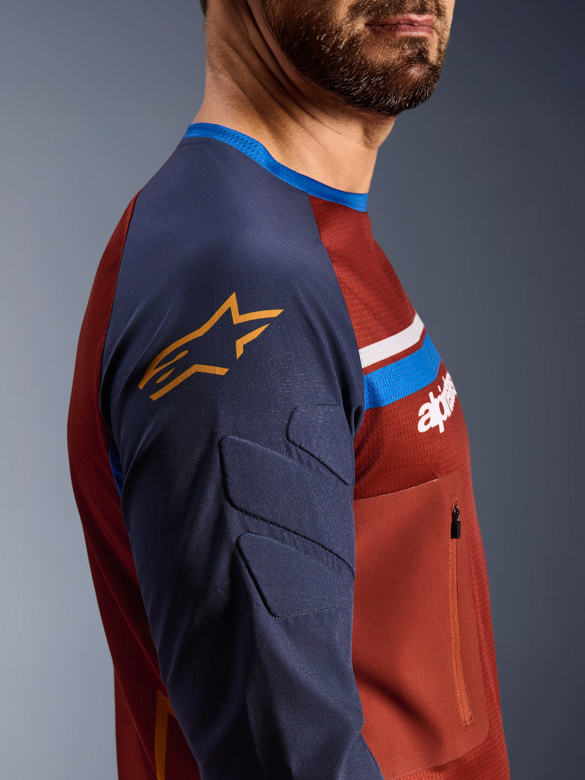Alpinestars Maxdura Dual Jersey, Rust Brown e Mood Indigo, vista laterale di profilo che mostra maniche imbottite con logo a stella giallo, costruzione del busto in rete con tasca sul petto con cerniera, abbigliamento tecnico da moto per guida adventure
