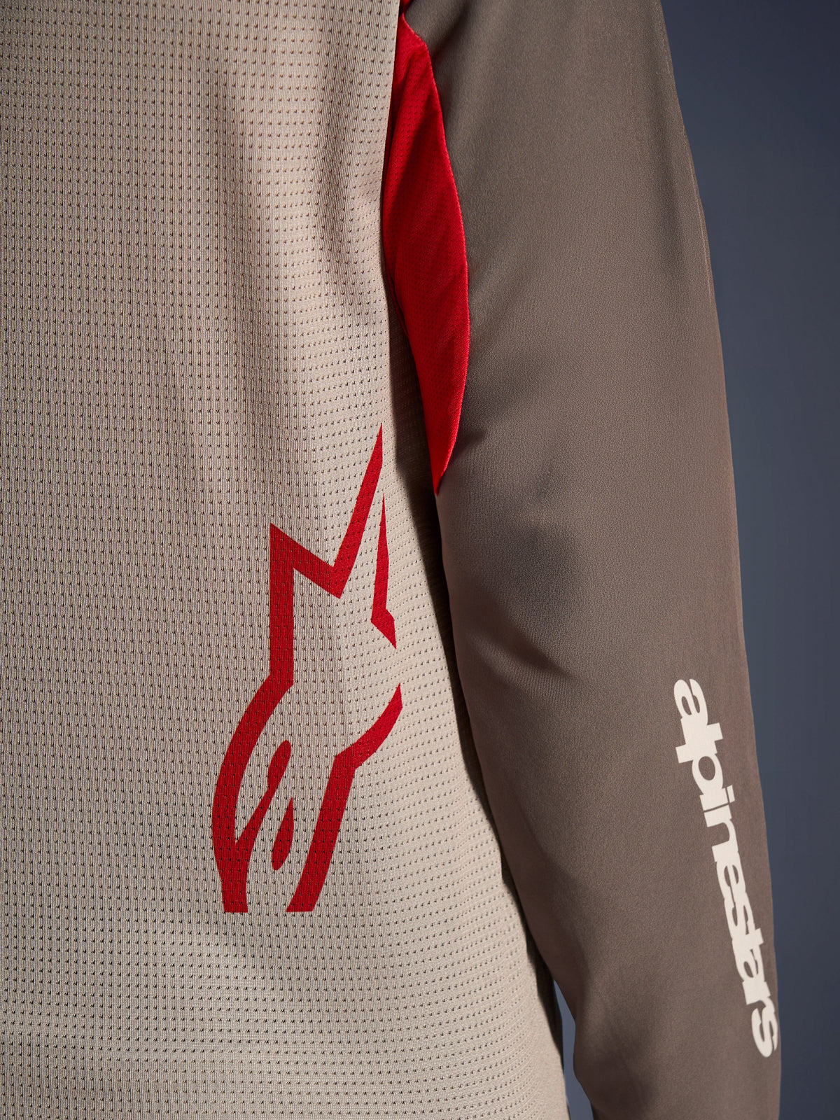 Alpinestars Maxdura Dual Jersey, Aluminum Walnut, vista ravvicinata del busto in mesh ventilato con logo a stella rosso e manica marrone resistente all'abrasione con scritta Alpinestars bianca, abbigliamento tecnico da moto adventure e dual-sport