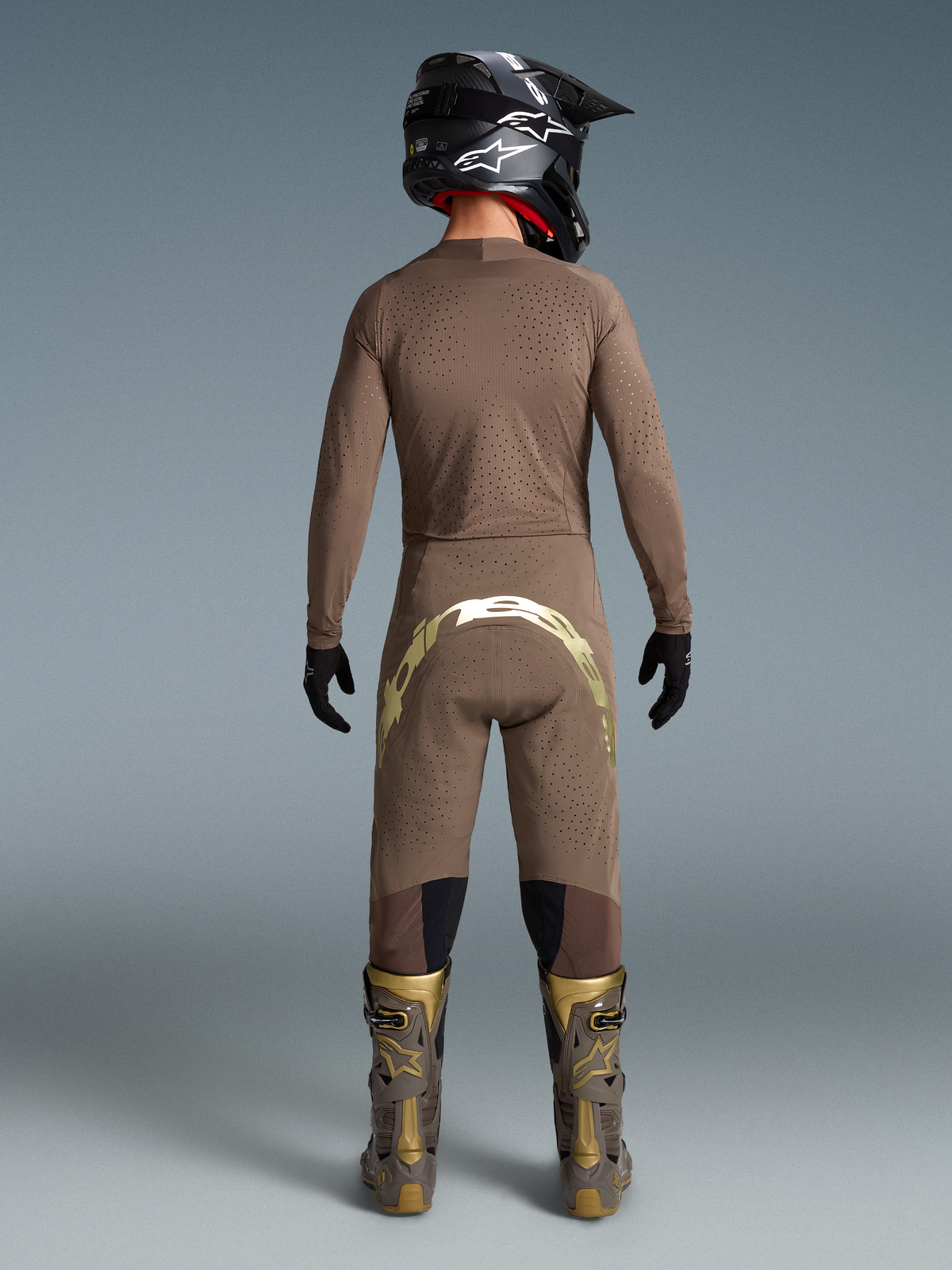 Completo motocross Alpinestars Limited Edition Supertech Air Gold, maglia e pantaloni ventilati marrone e oro, stivali Tech 10, visto da dietro.