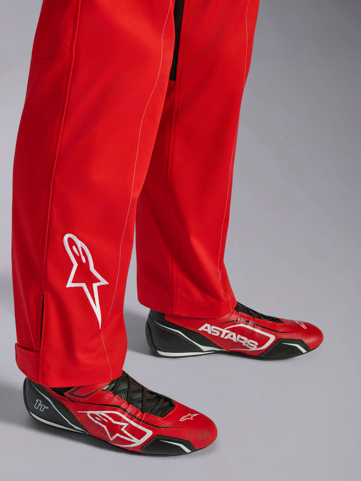 Alpinestars Kart Indoor V2 Suit, rossa, dettaglio fondo gamba con logo a stella bianco ricamato, indossata con scarpe da kart rosse e nere coordinate, materiale twill in policotone a strato singolo per karting ricreativo