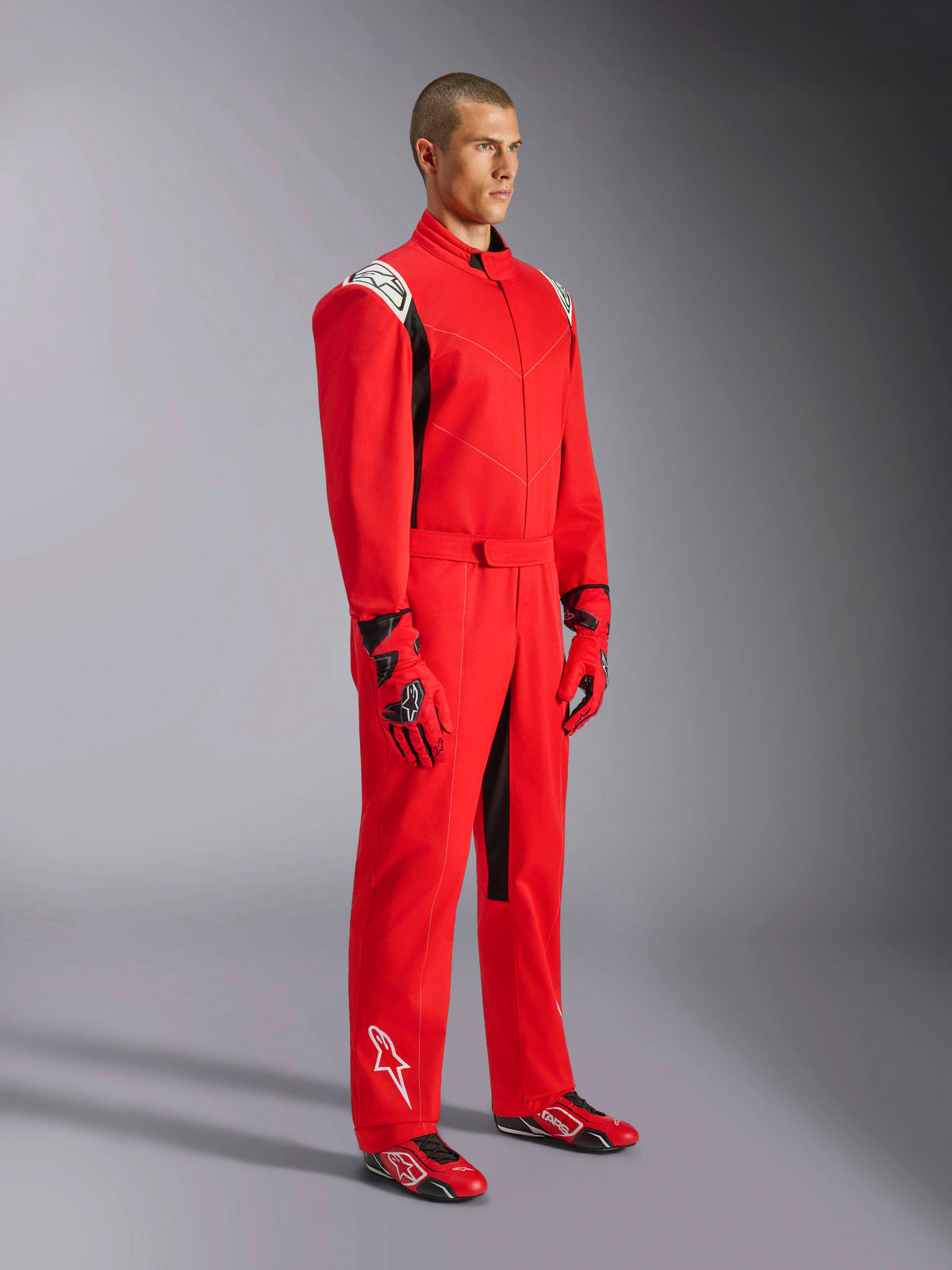 Alpinestars Kart Indoor V2 Suit, tuta da kart rossa, indossata da un modello con guanti e scarpe coordinati rossi e neri, loghi bianchi sulle spalle e sulla parte inferiore della gamba, dettagli neri, progettata per il karting ricreativo e le piste indoor