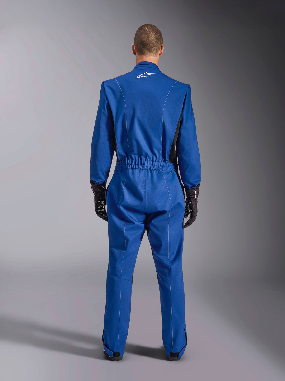 Alpinestars Kart Indoor V2 Suit, blu, vista posteriore, tuta da kart intera con logo bianco sulla parte superiore della schiena, vita elasticizzata e dettagli neri, indossata con guanti da corsa neri