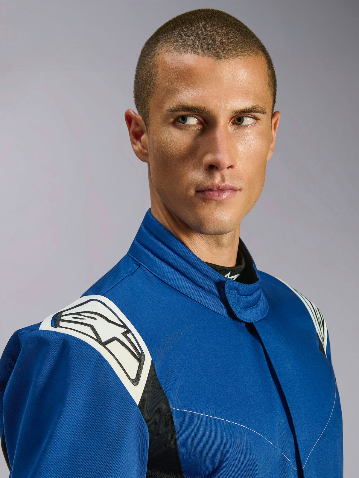 Alpinestars Kart Indoor V2 Suit, tuta da kart blu, primo piano di un modello maschile, pannelli bianchi sulle spalle con logo a stella nero, colletto ergonomico, twill a strato singolo resistente per karting ricreativo.