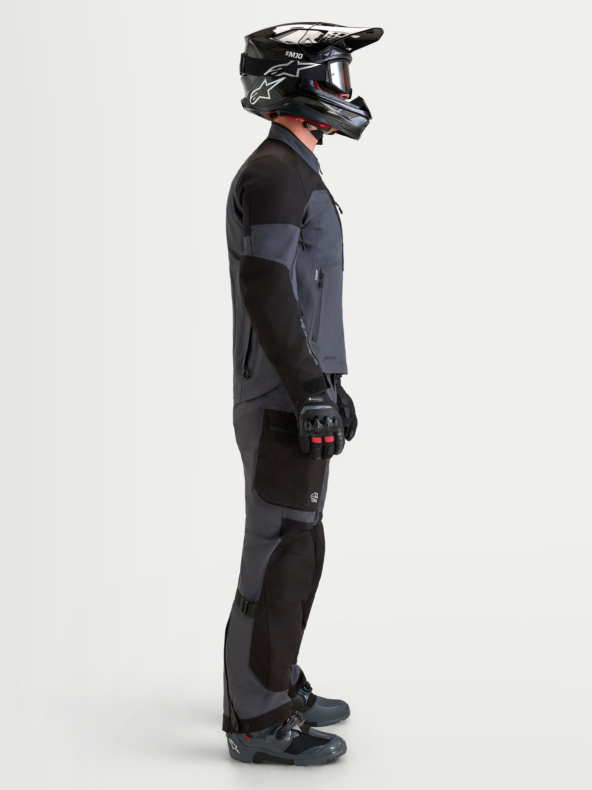 Alpinestars Arenis Gore-Tex Gear Set, completo da moto adventure da uomo in nero e grigio scuro, vista di profilo laterale di un modello che indossa casco e stivali coordinati, abbigliamento da guida impermeabile all-terrain