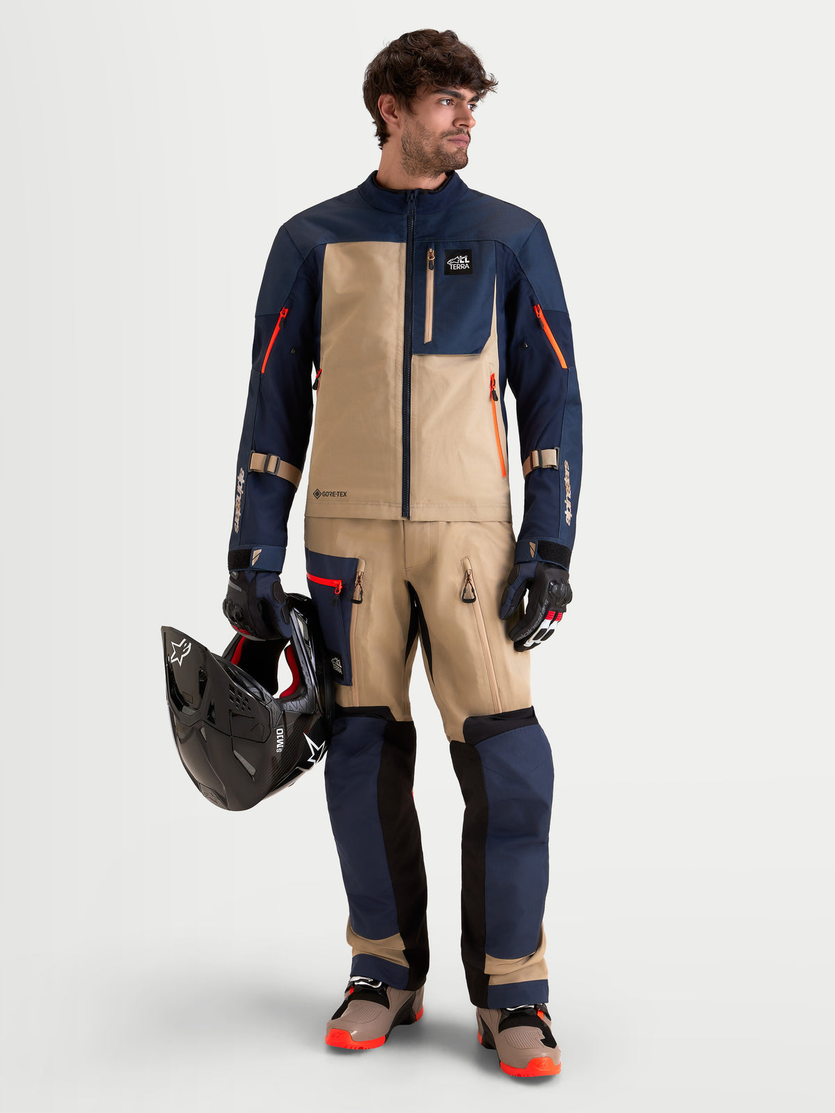 Alpinestars Arenis Gore-Tex Giacca, giacca da moto adventure da uomo in blu navy e beige alluminio, indossata da un modello che tiene un casco