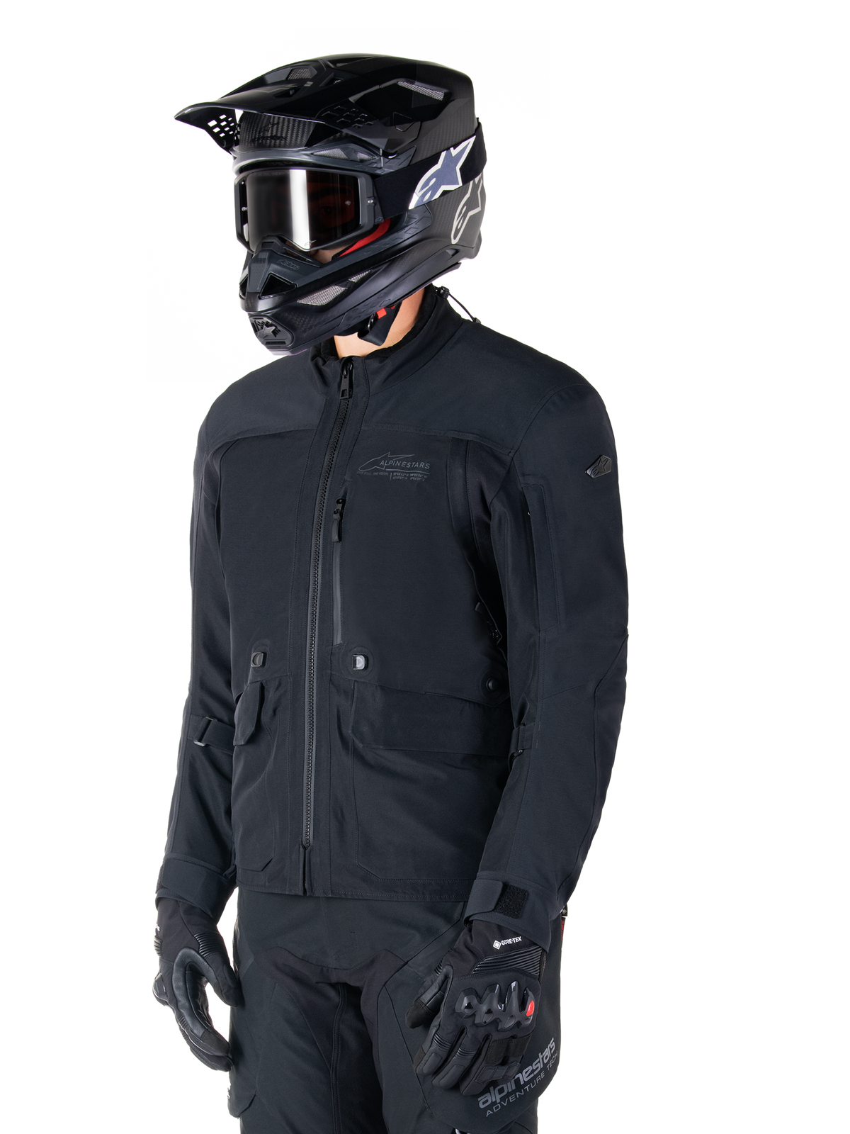 Giacca Alpinestars St-7 Prime GORE-TEX, giacca da moto nera, indossata da un pilota con casco e occhiali neri, dotata di ampie tasche cargo sul petto e guscio impermeabile laminato, abbigliamento premium per adventure touring e commuting
