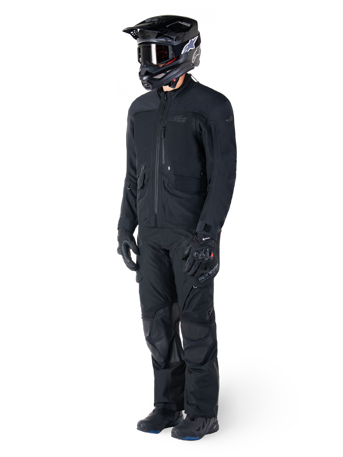 Motociclista che indossa la giacca Alpinestars St-7 Prime GORE-TEX in nero, completo coordinato da adventure touring con pantaloni neri abbinati, casco nero con maschera e guanti, caratterizzato da un design essenziale e funzionale per prestazioni in ogni condizione atmosferica.