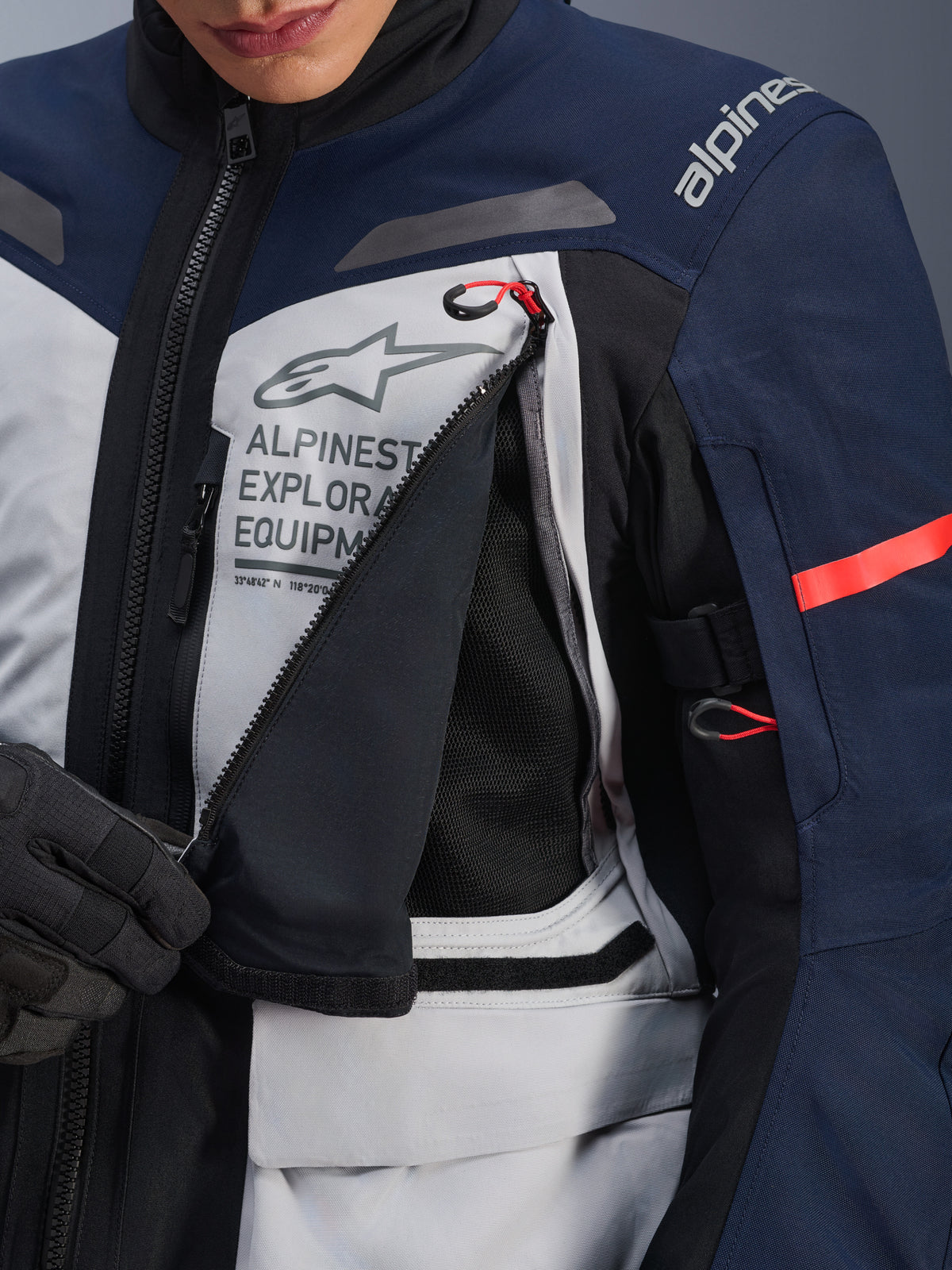 Giacca Alpinestars ST-7 2L GORE-TEX, giacca adventure touring, Ice Gray, blu scuro e nero, vista dettagliata del pannello di ventilazione sul petto aperto che mostra la rete nera, con logo Alpinestars Exploration Equipment e tiranti con accenti rossi