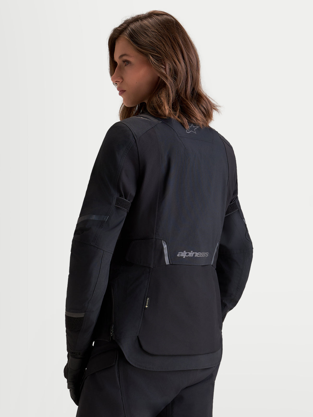Alpinestars Stella St-7 V2 2L Gore-Tex Giacca, giacca da moto adventure da donna in nero, vista posteriore a tre quarti indossata da una modella che mostra la struttura in tessuto impermeabile e i dettagli con logo riflettente
