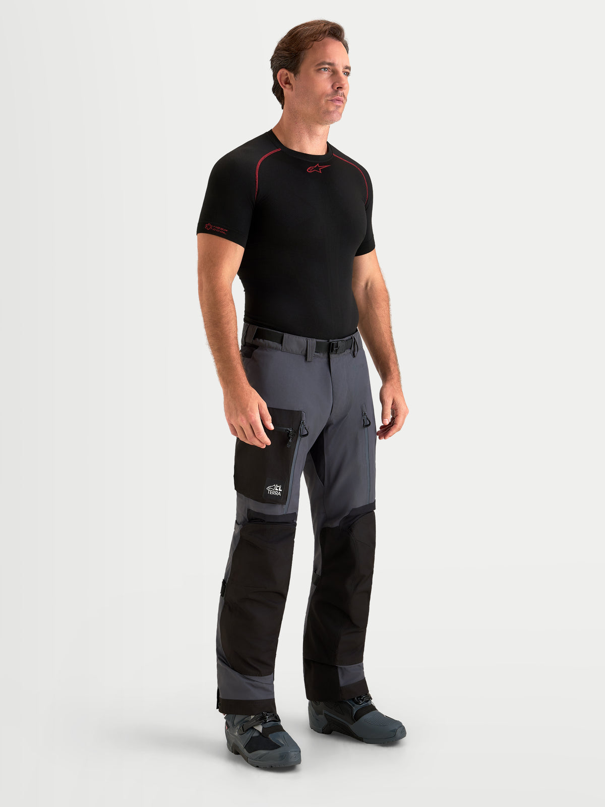Alpinestars Arenis Gore Tex Pantaloni, pantaloni da moto adventure da uomo, grigio scuro e nero, vista anteriore su un modello che indossa abbigliamento coordinato e struttura in tessuto impermeabile