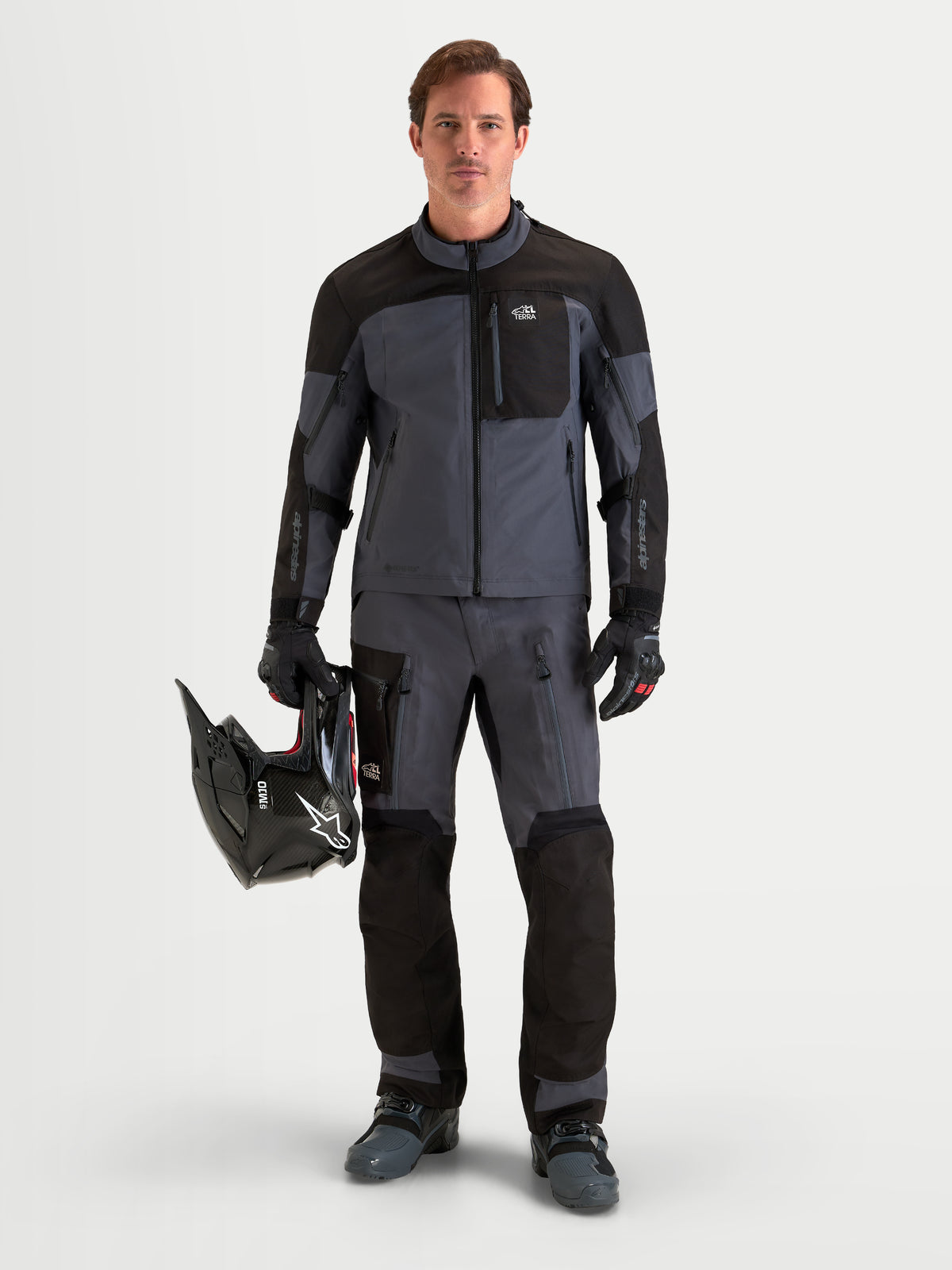 Alpinestars Arenis Gore-Tex Pantaloni, pantaloni da moto adventure da uomo, nero e grigio scuro, vista frontale su un modello che indossa attrezzatura coordinata, casco e abbigliamento da guida impermeabile in tessuto