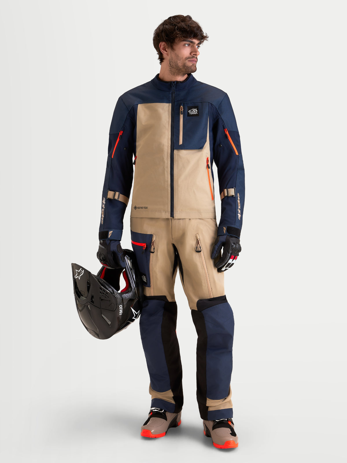 Alpinestars Arenis Gore-Tex Pantaloni, pantaloni da moto adventure da uomo in blu notte e alluminio, indossati da un modello che tiene un casco come parte di un abbigliamento ADV abbinato