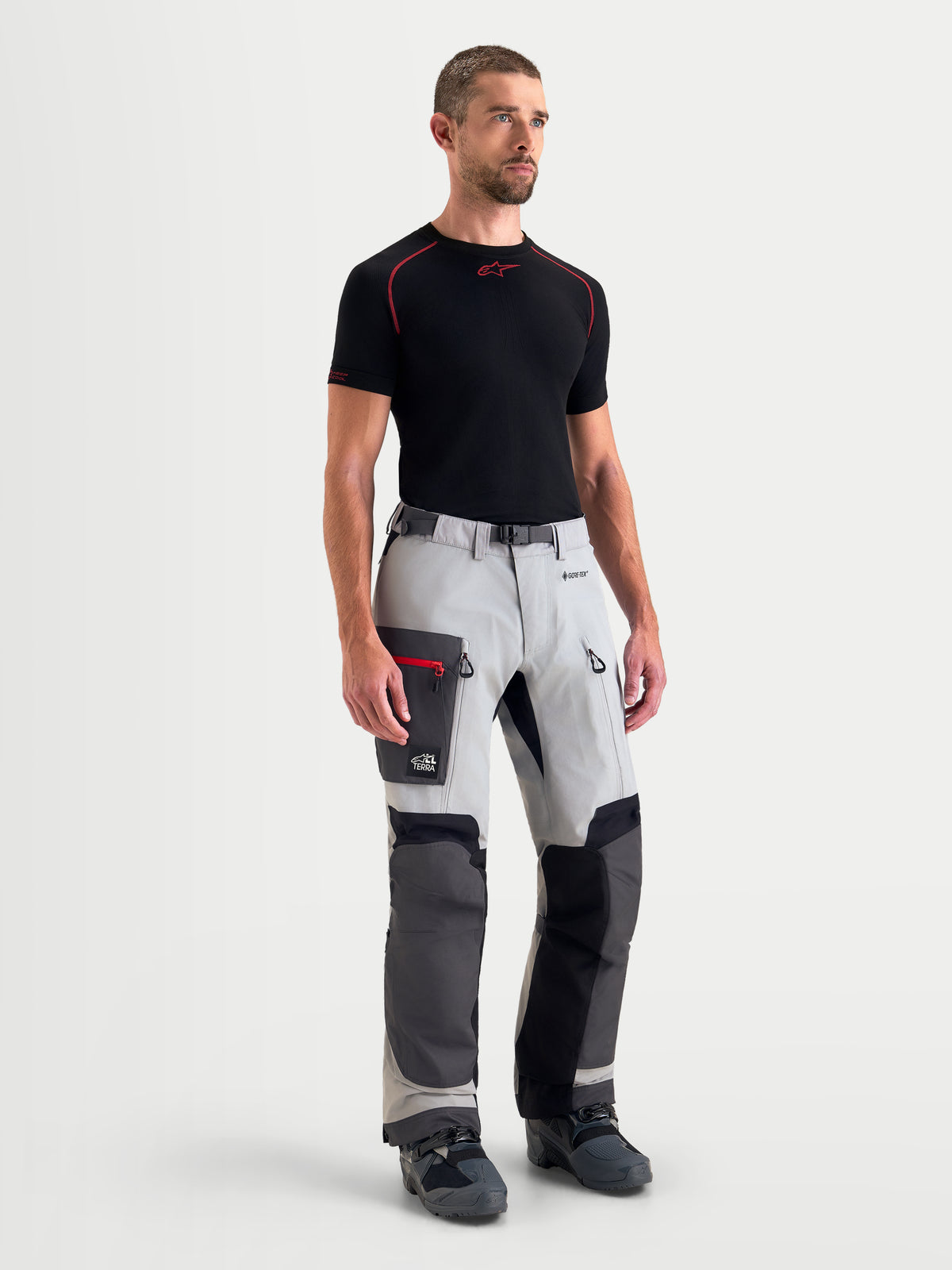 Alpinestars Arenis Gore-Tex Pantaloni, pantaloni da moto adventure da uomo in grigio medio, grigio scuro e nero, vista frontale su un modello che indossa abbigliamento da guida impermeabile con tasche cargo