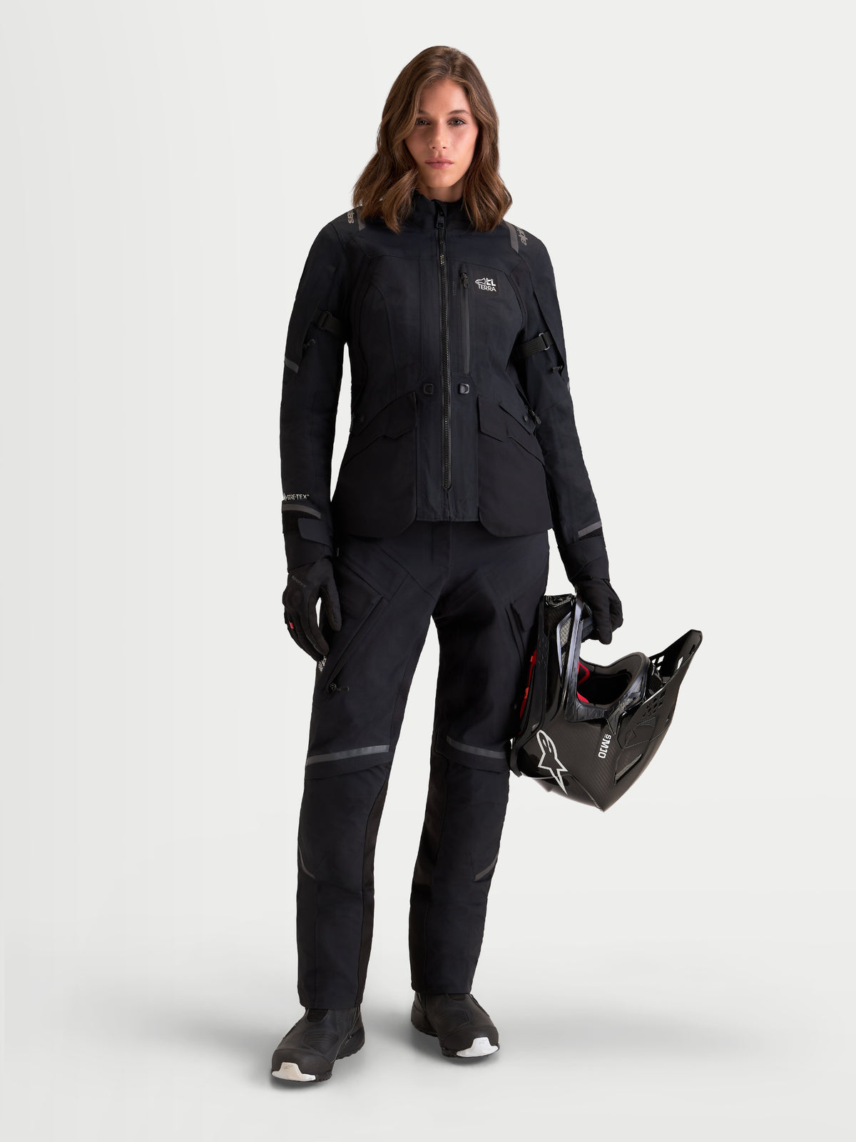Alpinestars Stella ST-7 V2 2L Gore-Tex Pantaloni, pantaloni da moto touring da donna, colore nero, vista frontale su una modella che indossa l'equipaggiamento coordinato e tiene un casco, con struttura in tessuto impermeabile